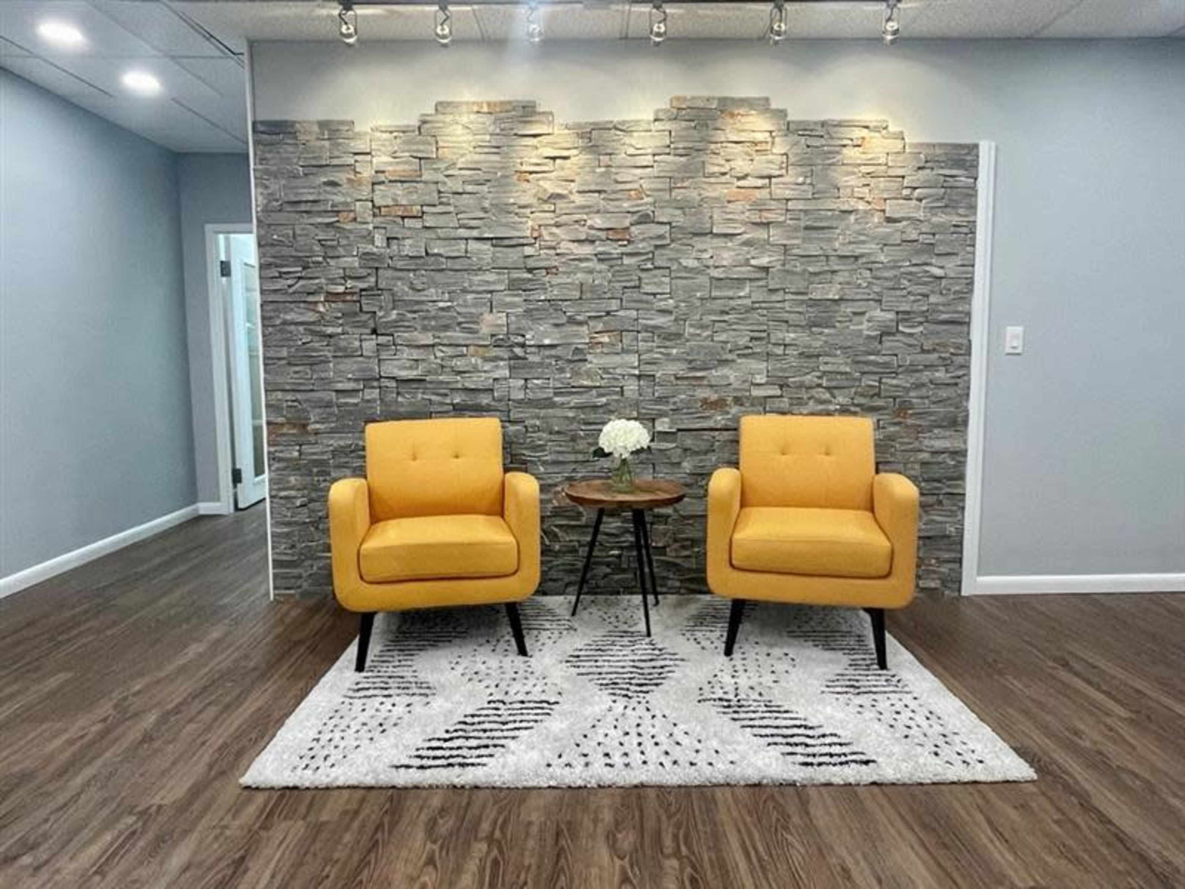 A pair of yellow armchairs positioned in front of a stone wall, accompanied by a small round table and a floral arrangement on it.