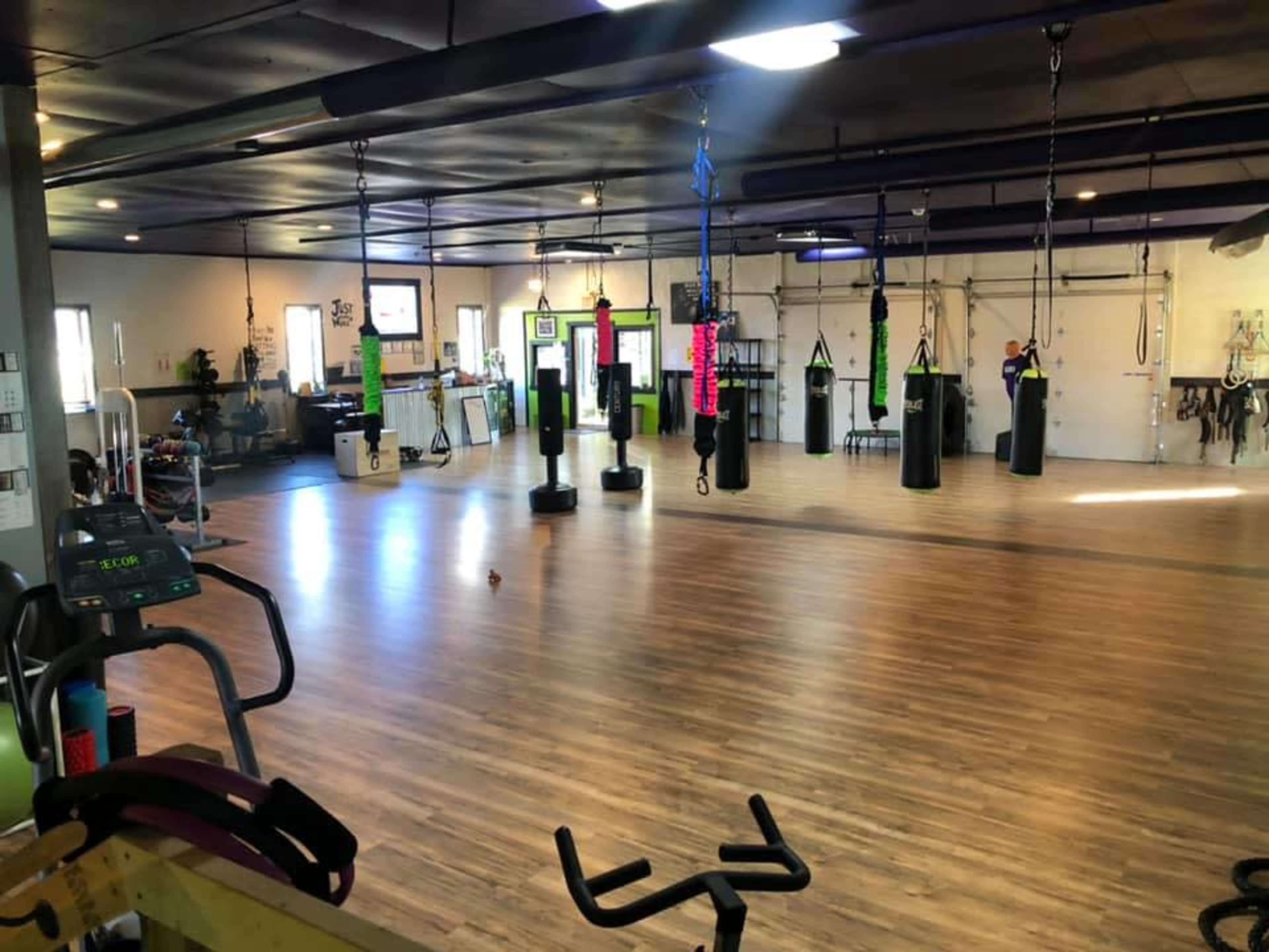 A spacious gym with various punching bags hanging from the ceiling and exercise equipment positioned around the wooden floor.