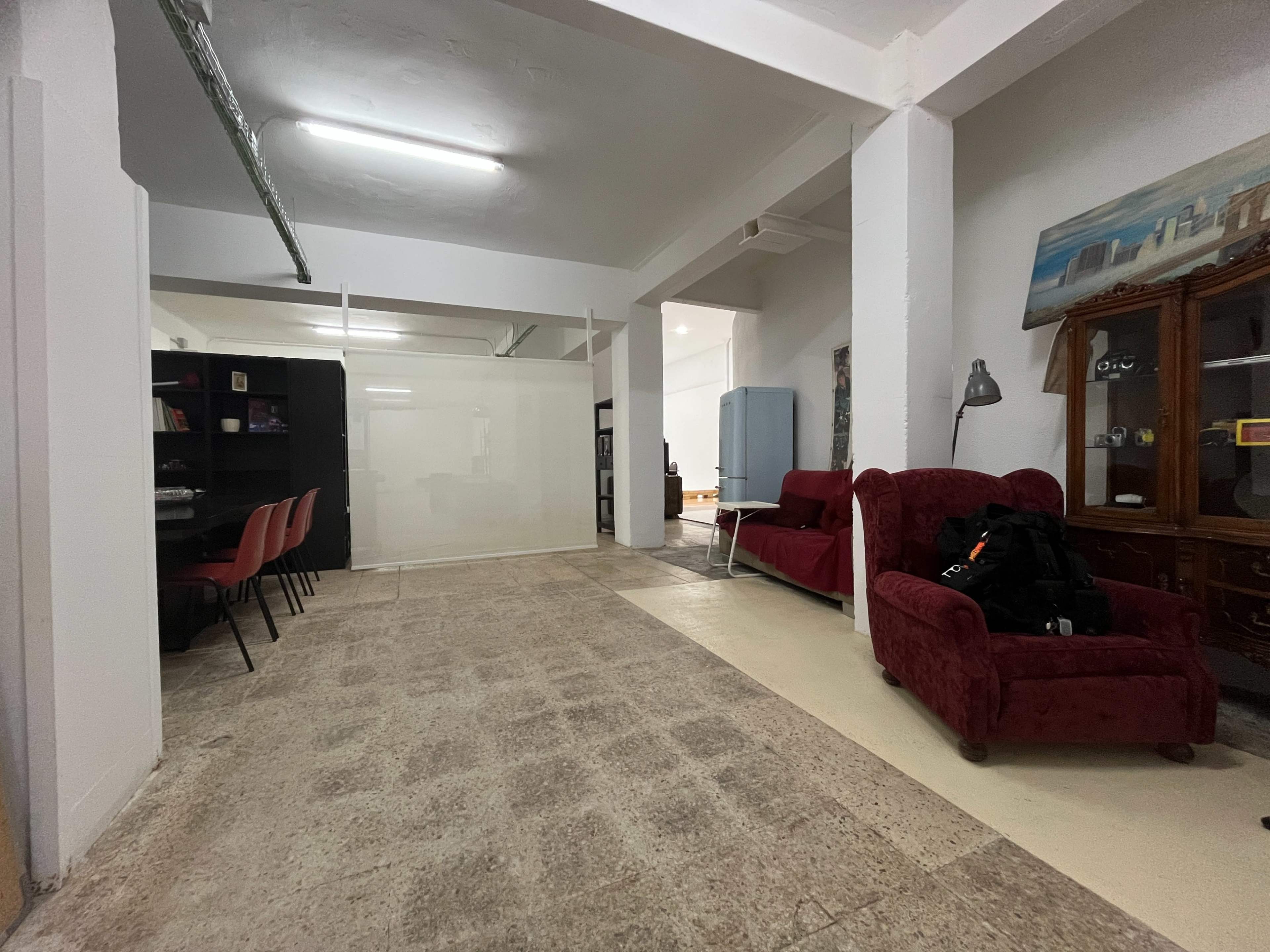 The image shows an open interior space with a seating area featuring two red couches, a glass partition separating sections, and a dining table with chairs in the background.