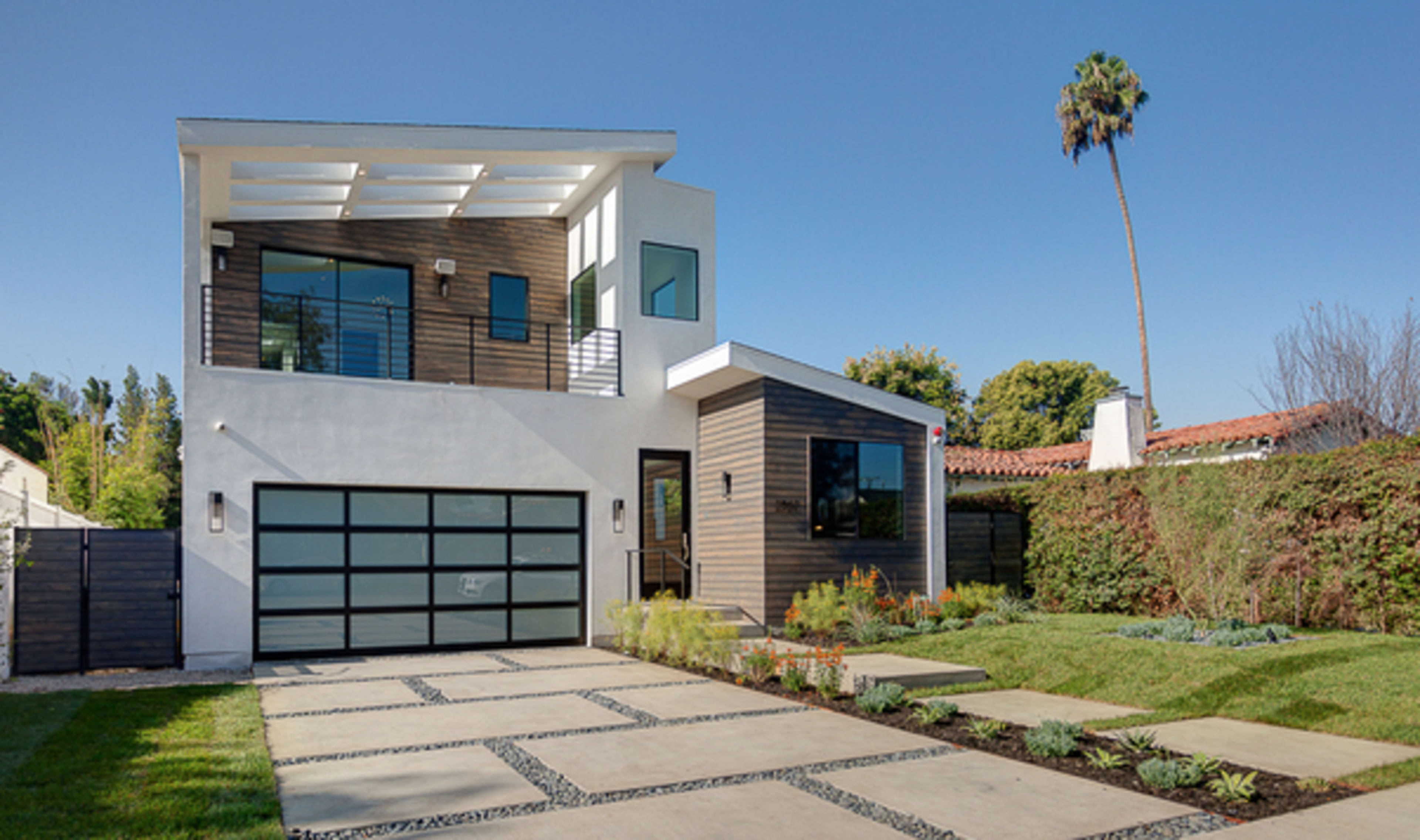 A modern two-story house with a flat roof, a large garage door, and a landscaped front yard.