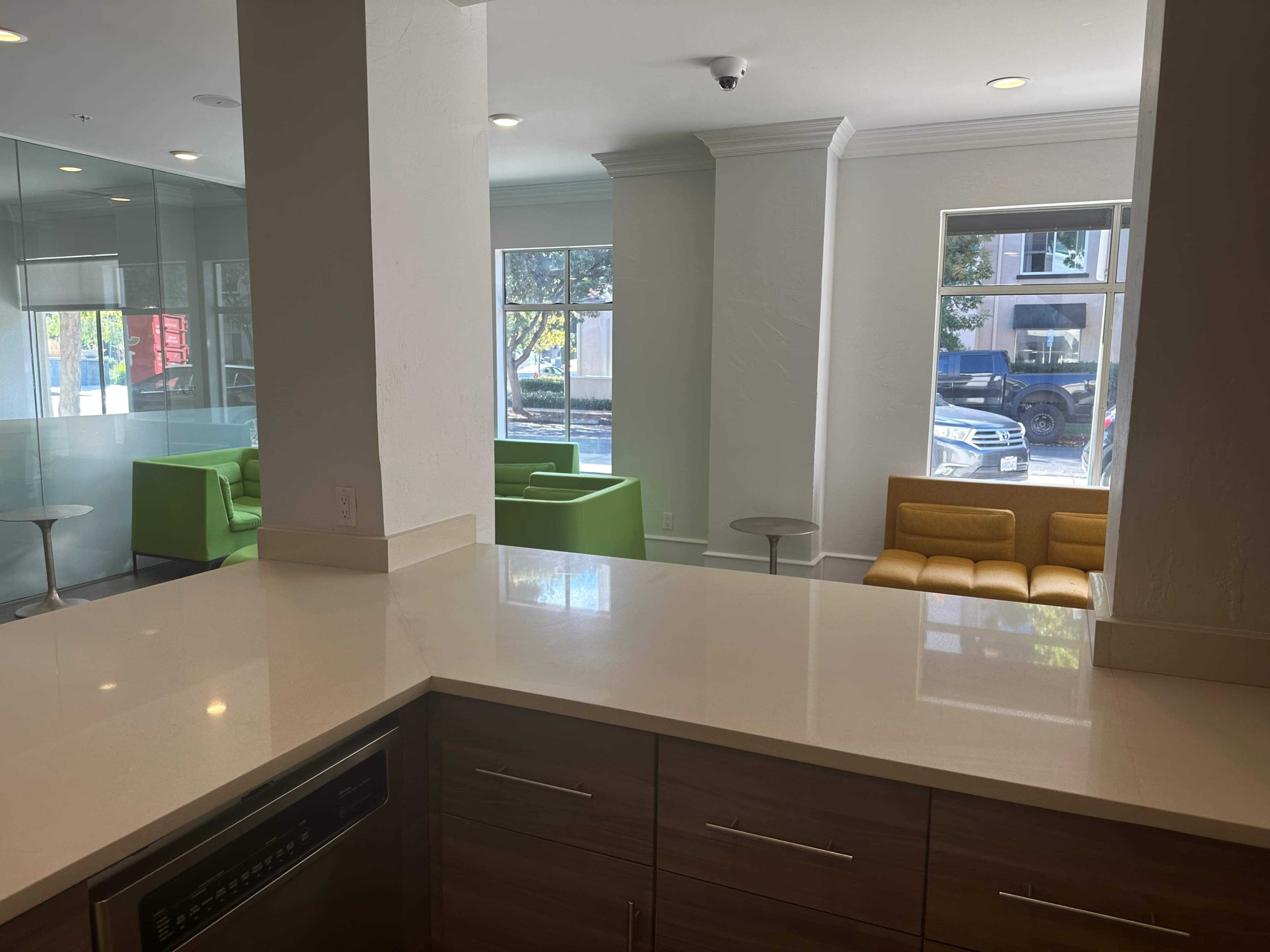 A modern interior space with a kitchen view, featuring a countertop, stainless steel appliances, and a lounge area with green and orange seating.