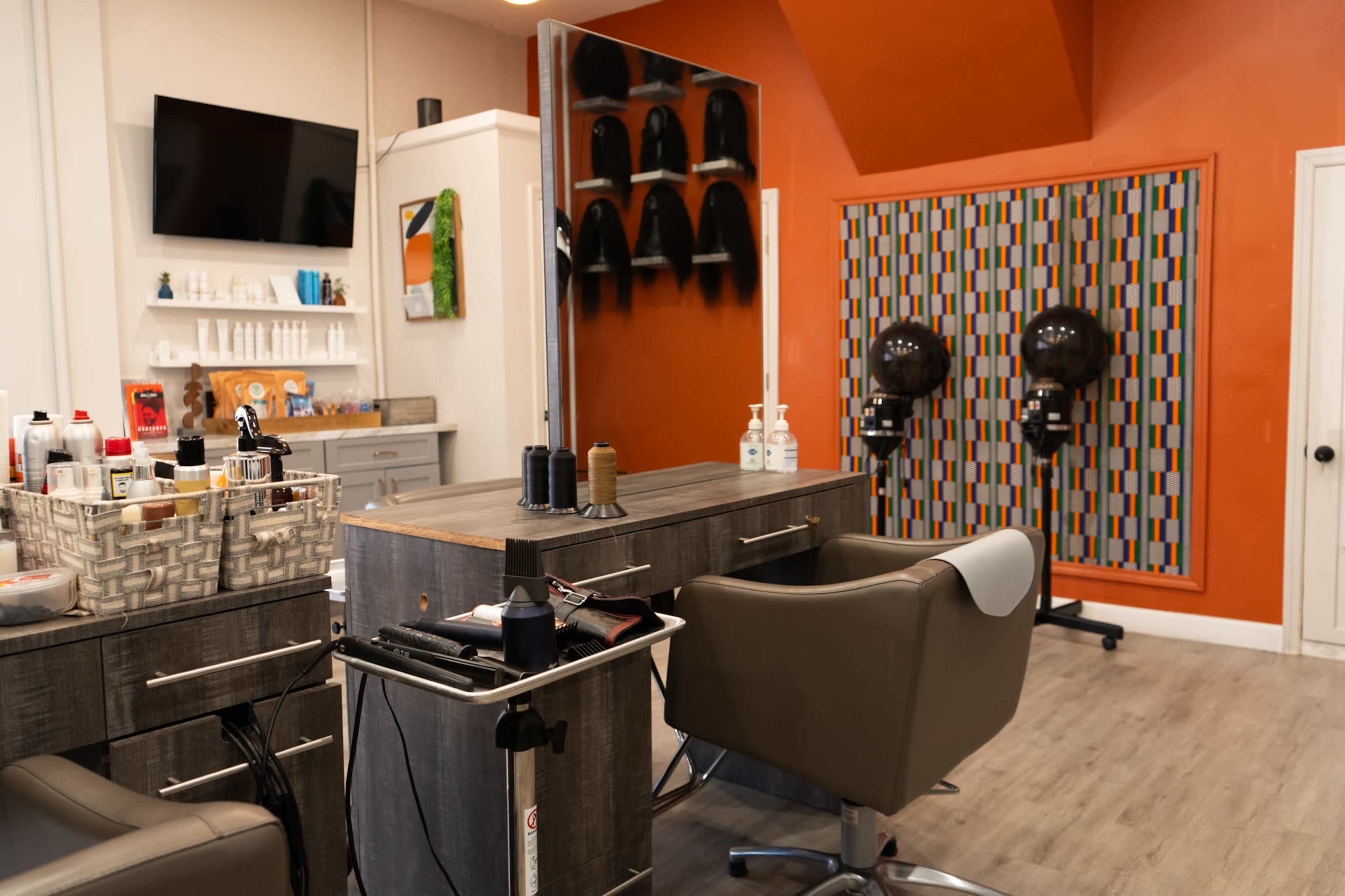 The image shows a modern hair salon interior featuring styling chairs, a mirrored wall, shelves of hair products, and two hair dryers mounted on the wall.