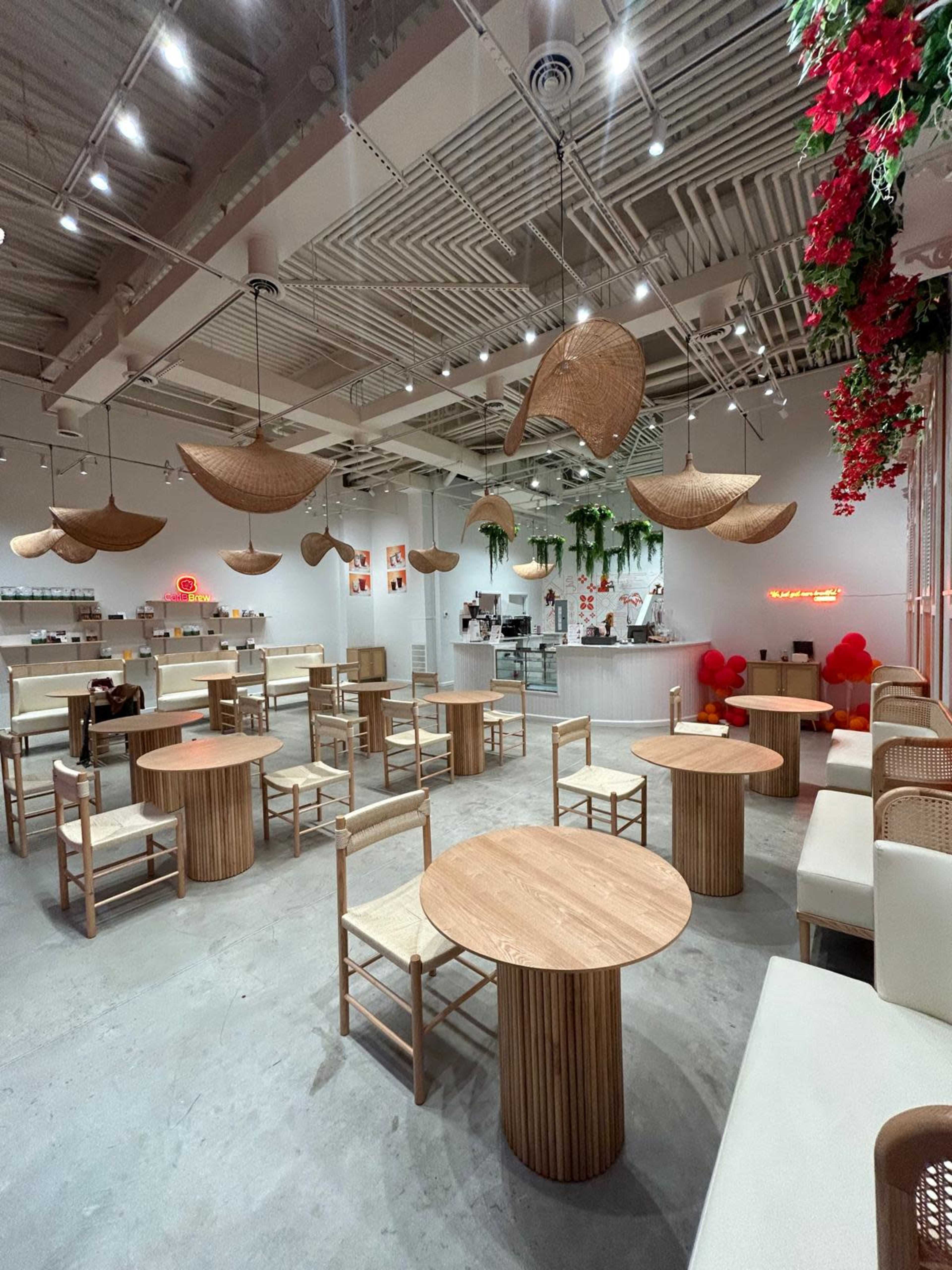 The image shows a modern café interior with wooden tables and chairs, hanging light fixtures, and decorative plants.