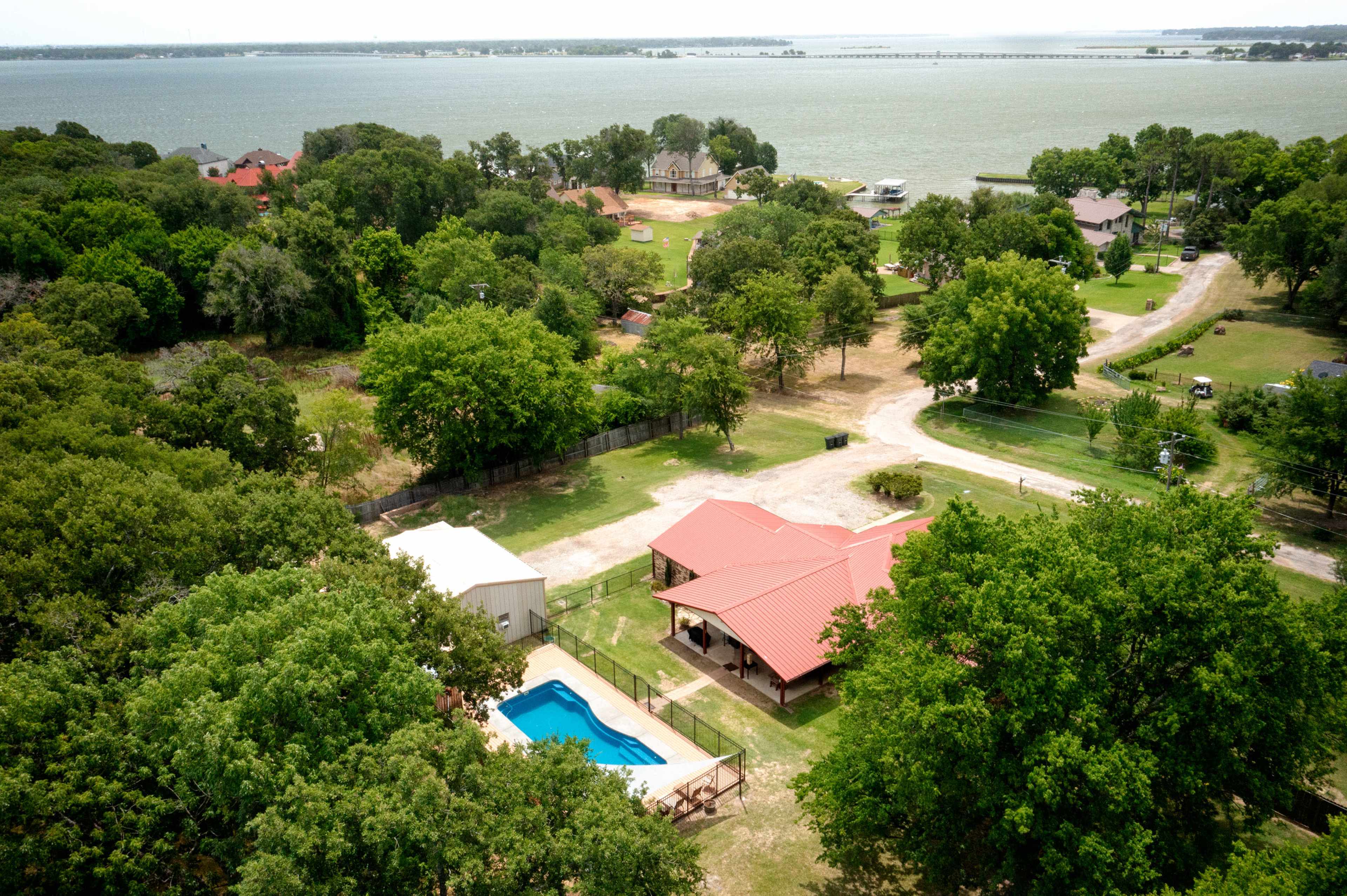 Aerial view of a property featuring a pool, surrounded by trees and near a body of water.
