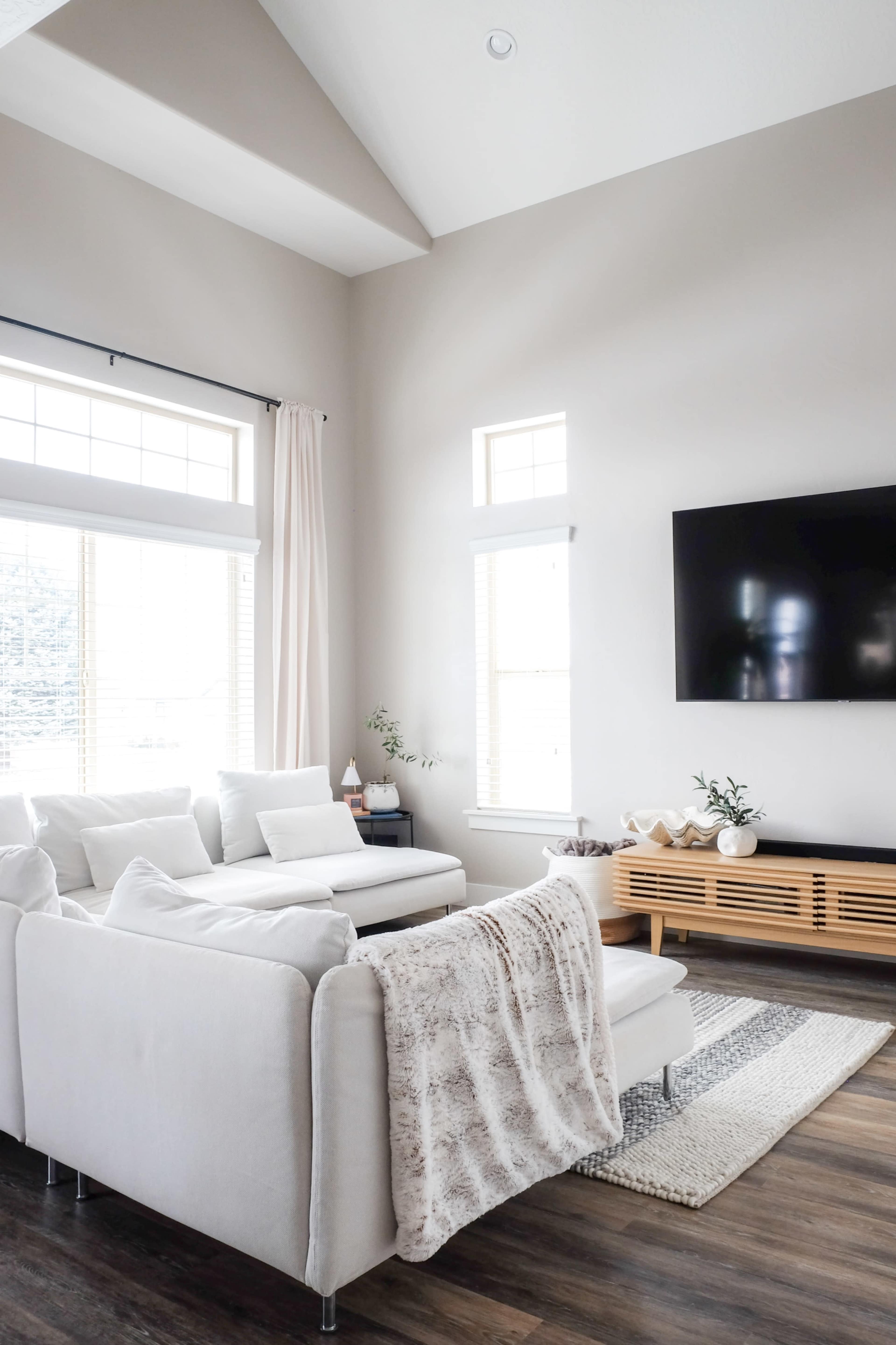 A modern living room featuring a large white sectional sofa, a wooden media console, and natural light streaming through the windows.