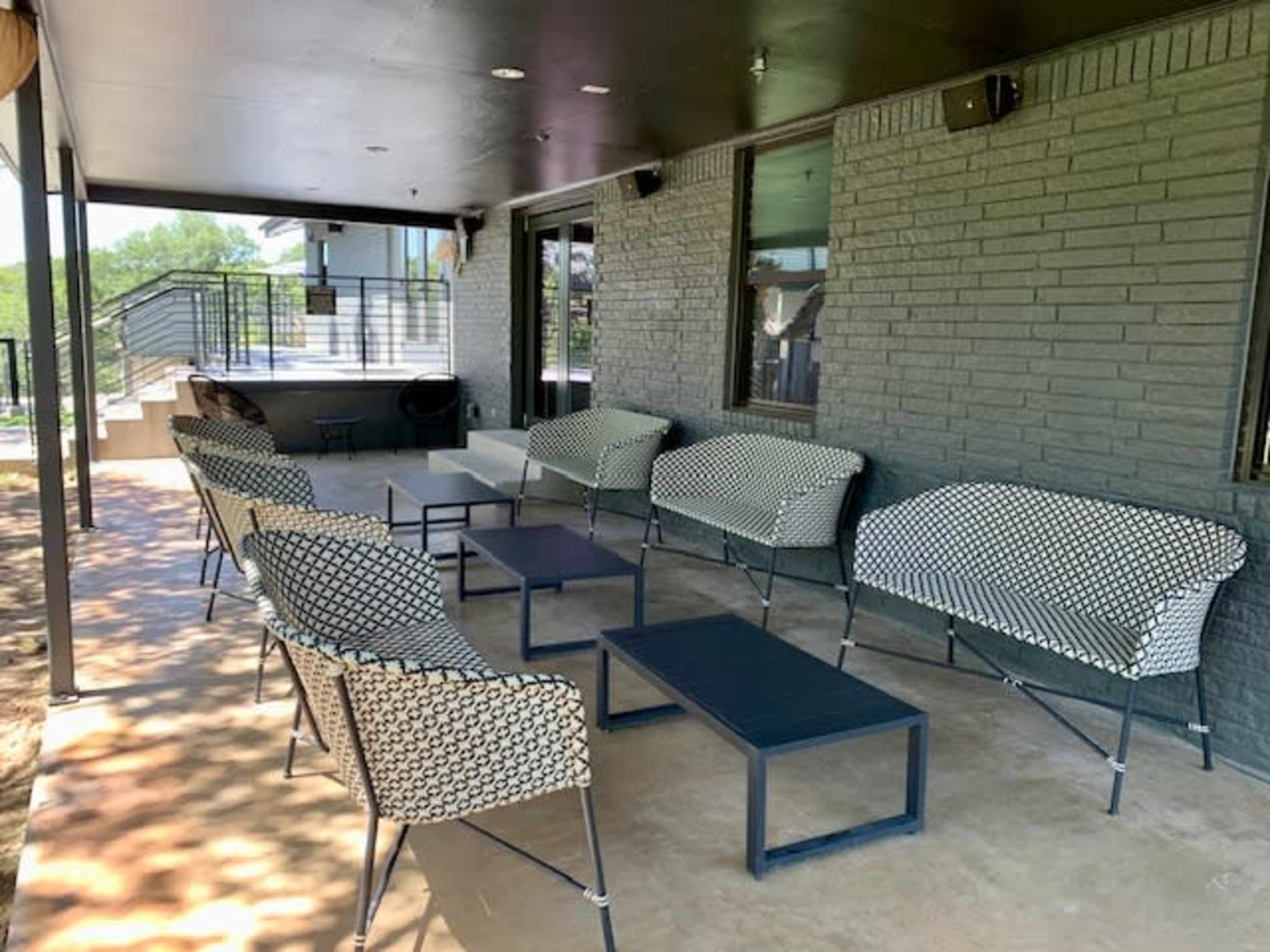The image shows an outdoor seating area featuring several patterned chairs and tables arranged on a concrete surface beneath a black overhang.