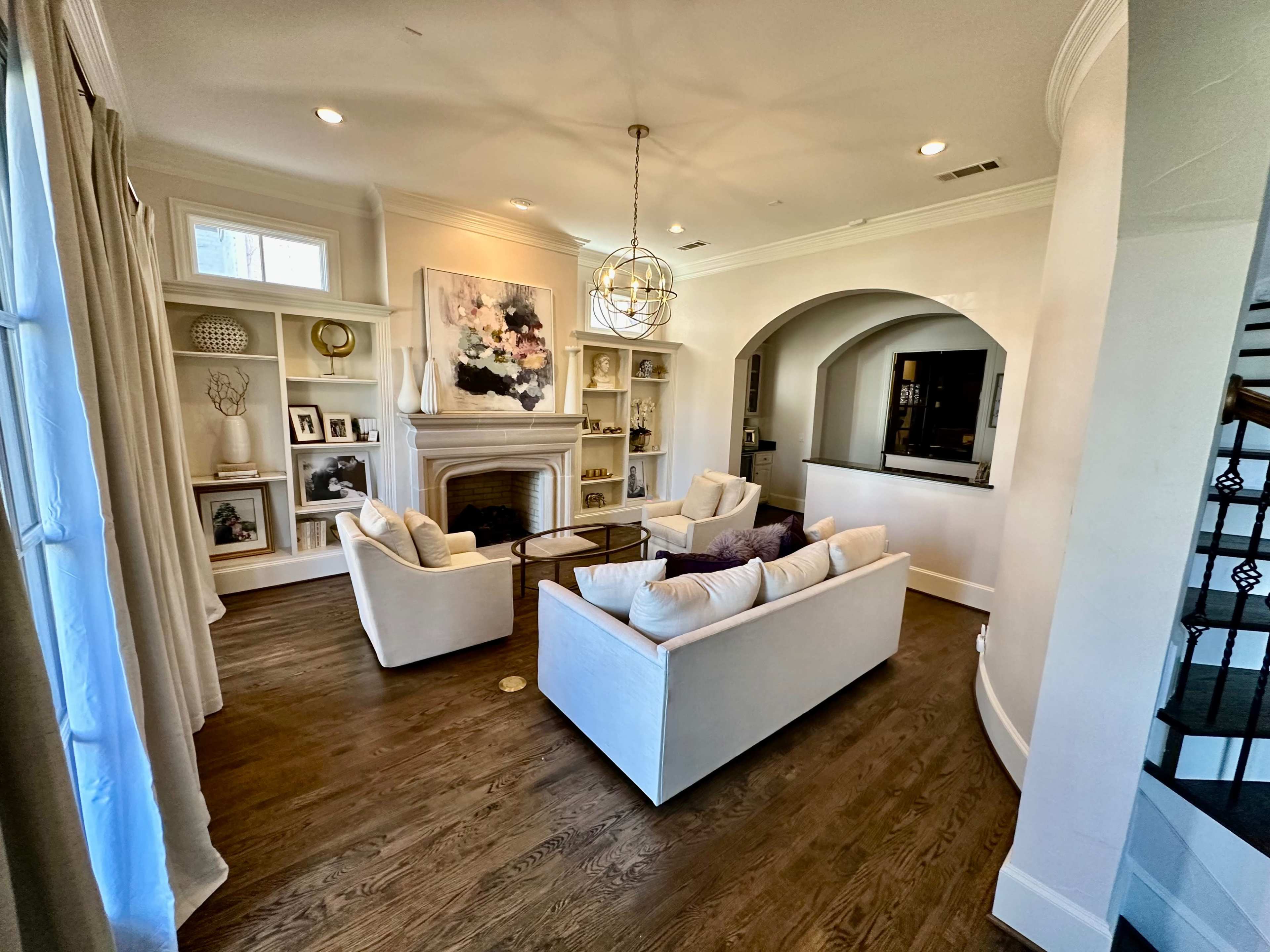 The image shows a living room featuring two white couches facing a fireplace, with built-in shelves displaying decor and a large artwork on the wall.