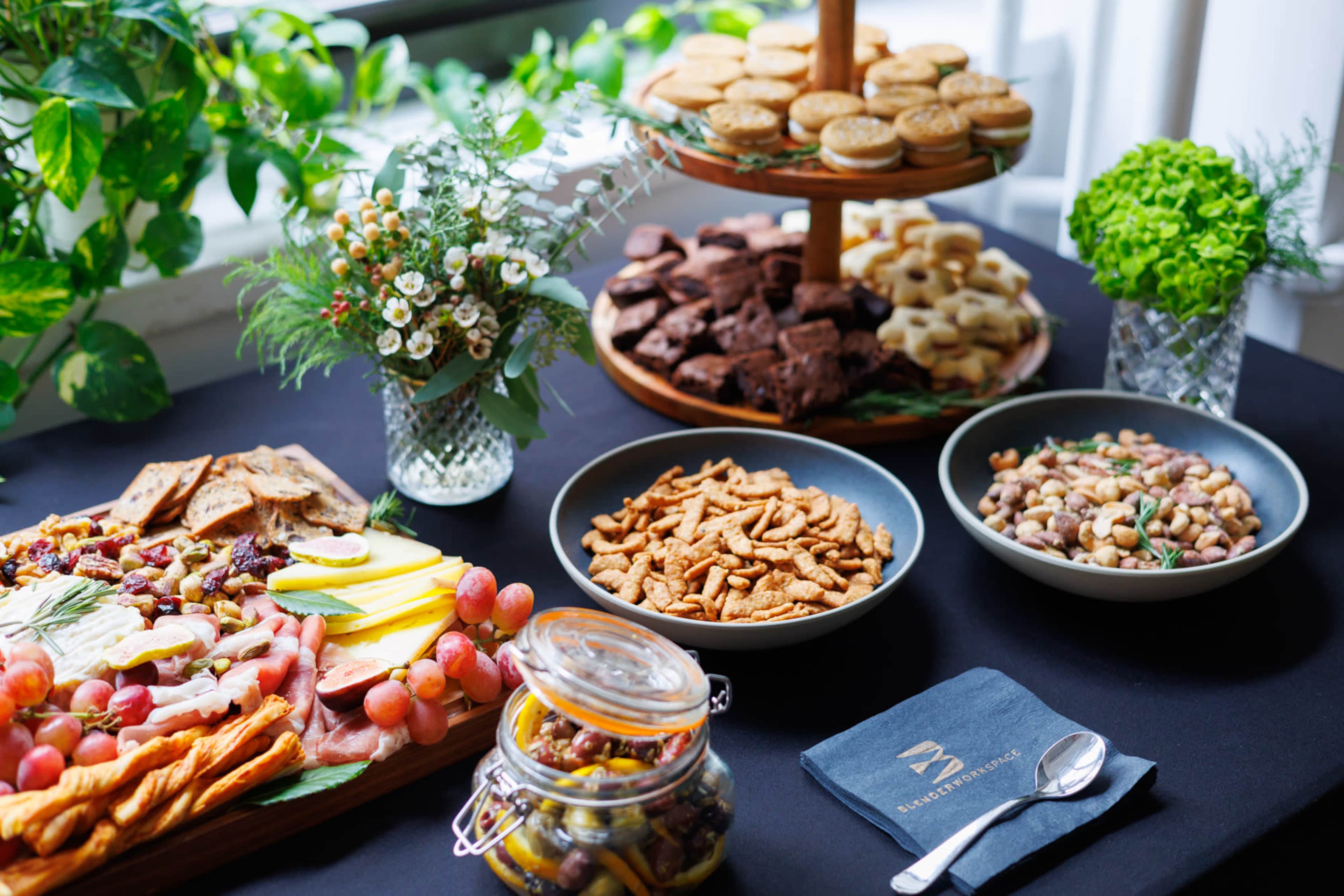 The image shows a buffet table featuring a variety of foods, including a colorful spread of fruits, snacks, and baked goods arranged on wooden platters and bowls.