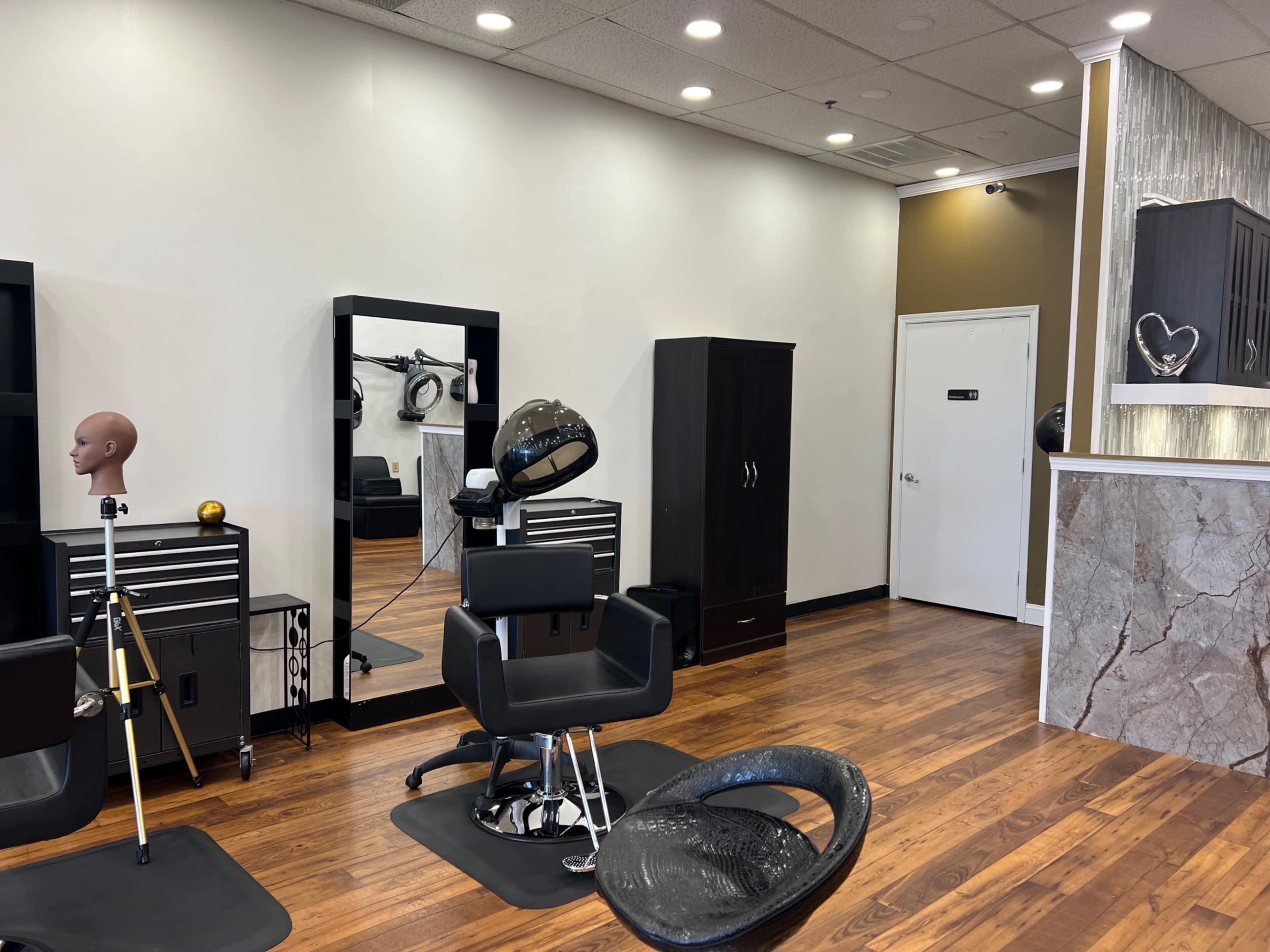 A well-lit hair salon interior featuring styling chairs, a mirror, and storage cabinets against wooden flooring.