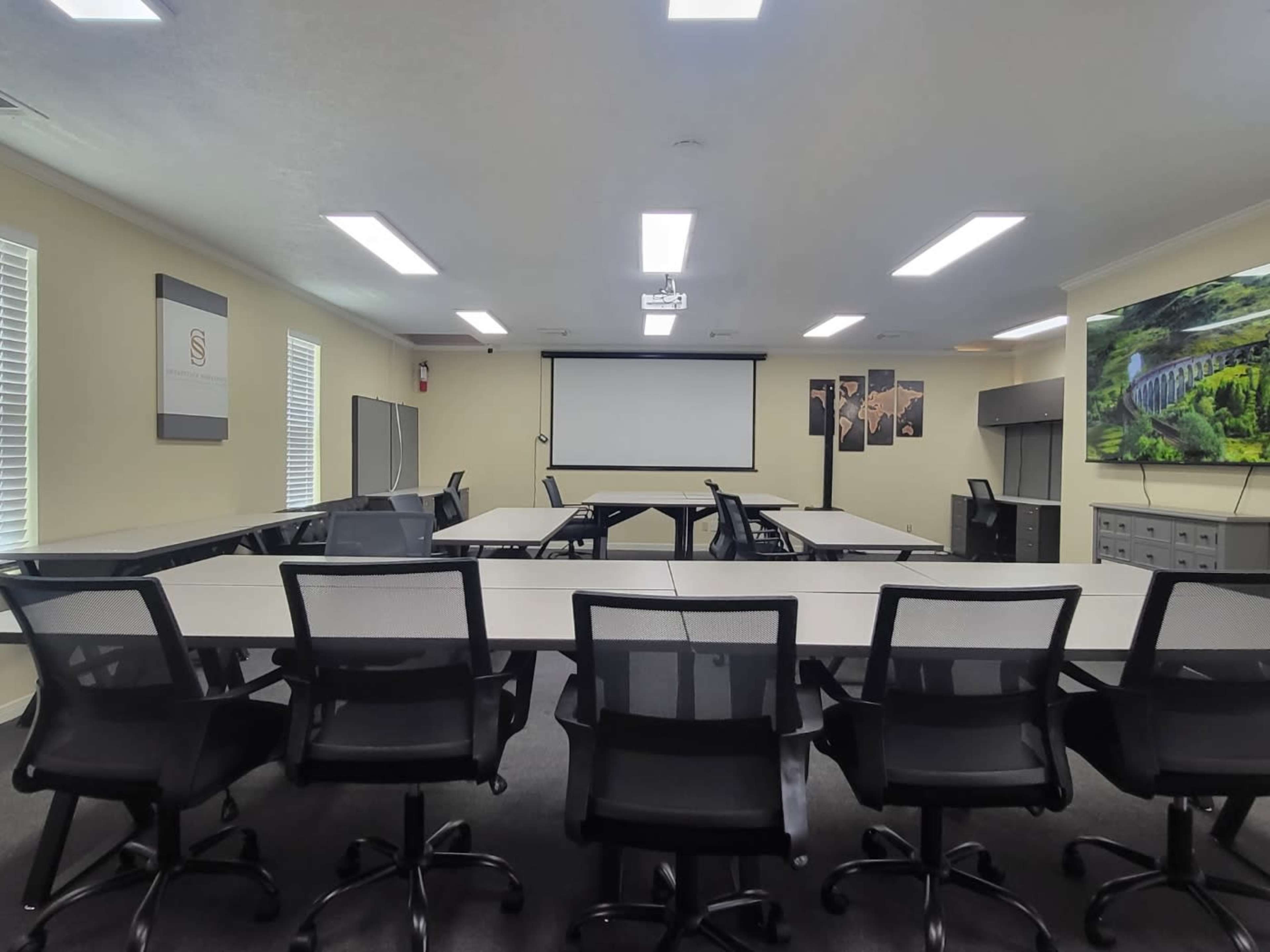 A conference room equipped with multiple tables, office chairs, a projector screen, and a large display on the wall.