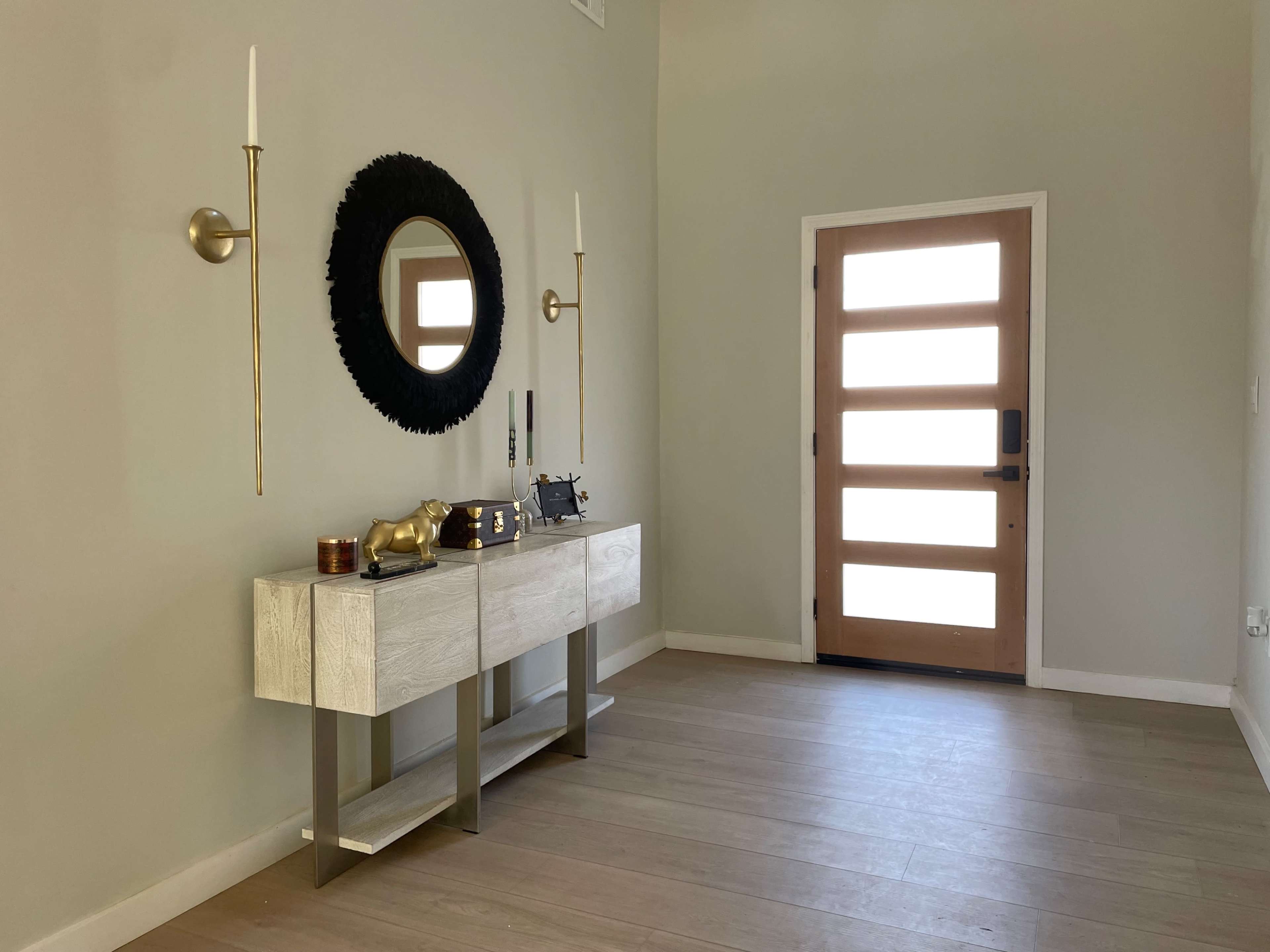 A modern entryway with a wooden door, a console table, a round mirror, and wall sconces.