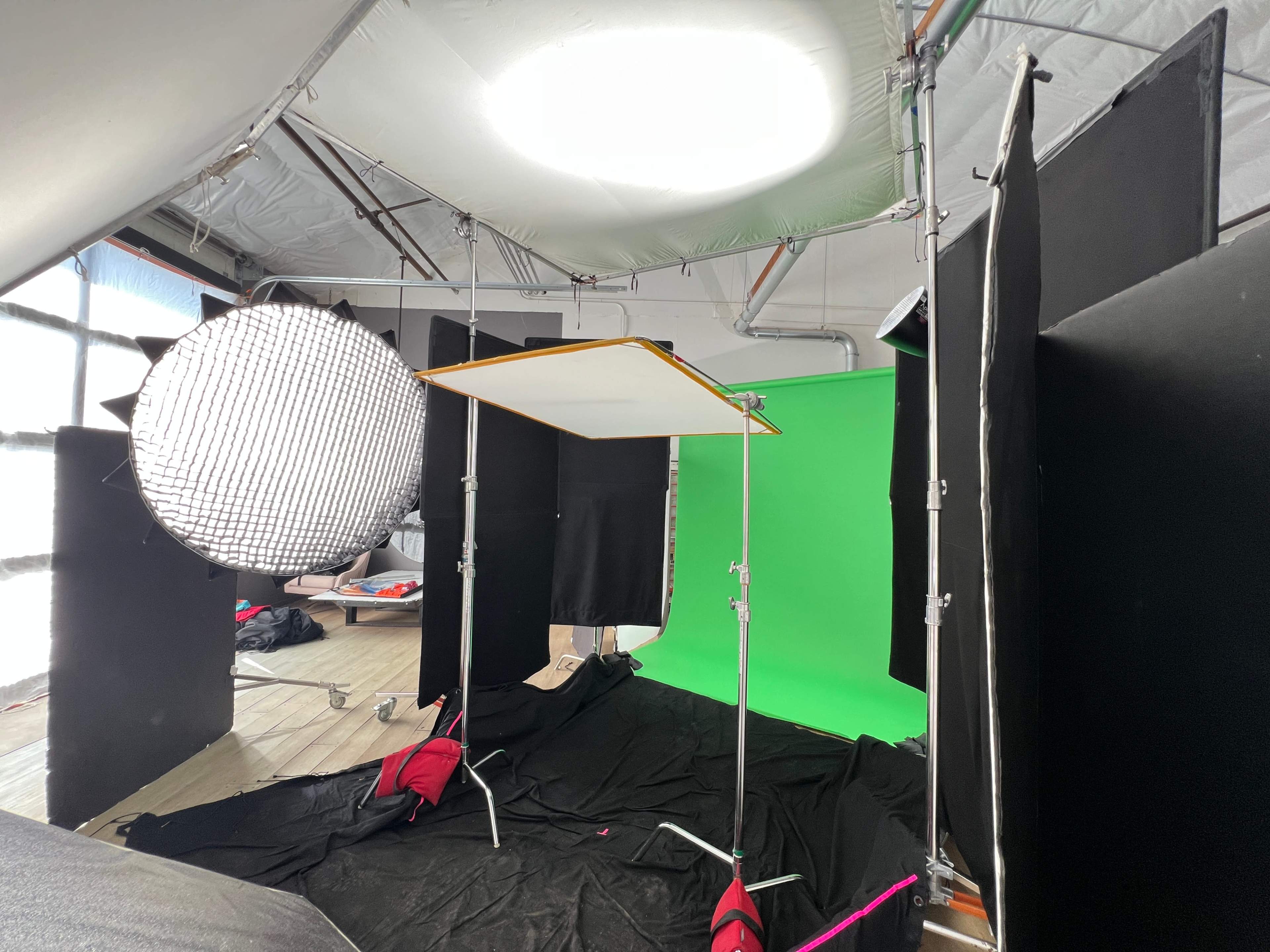The image shows a studio setup with a green screen surrounded by black backdrop panels and lighting equipment.