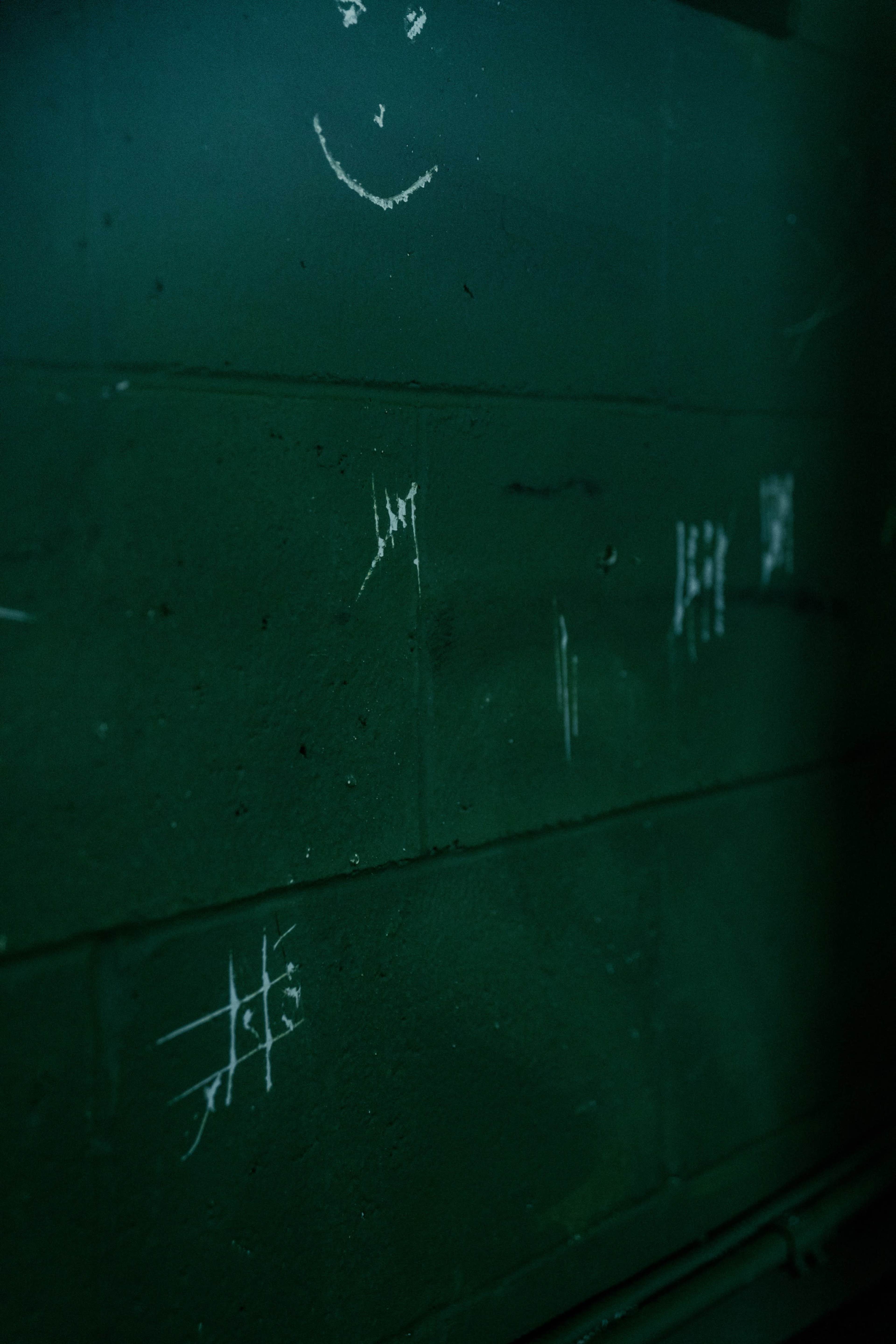 A dark green wall with white chalk or scratch markings, including a simple smiley face and various lines or tally marks.
