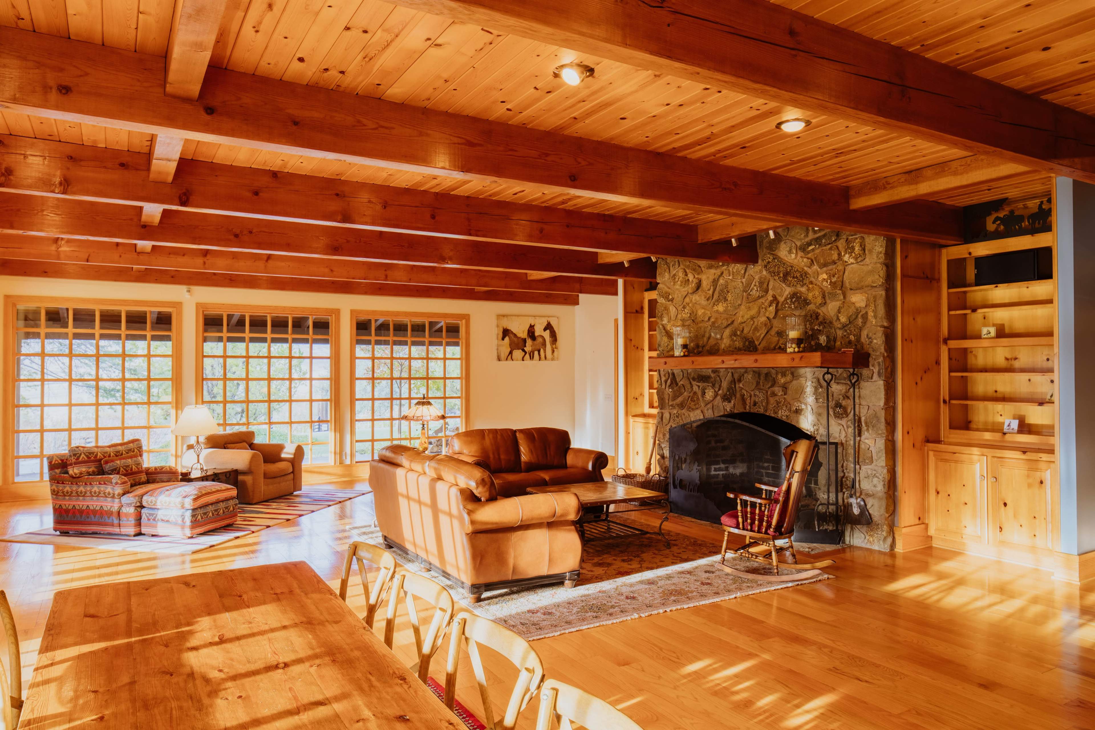 A cozy living room with wooden beams, a stone fireplace, and large windows that allow natural light to fill the space.