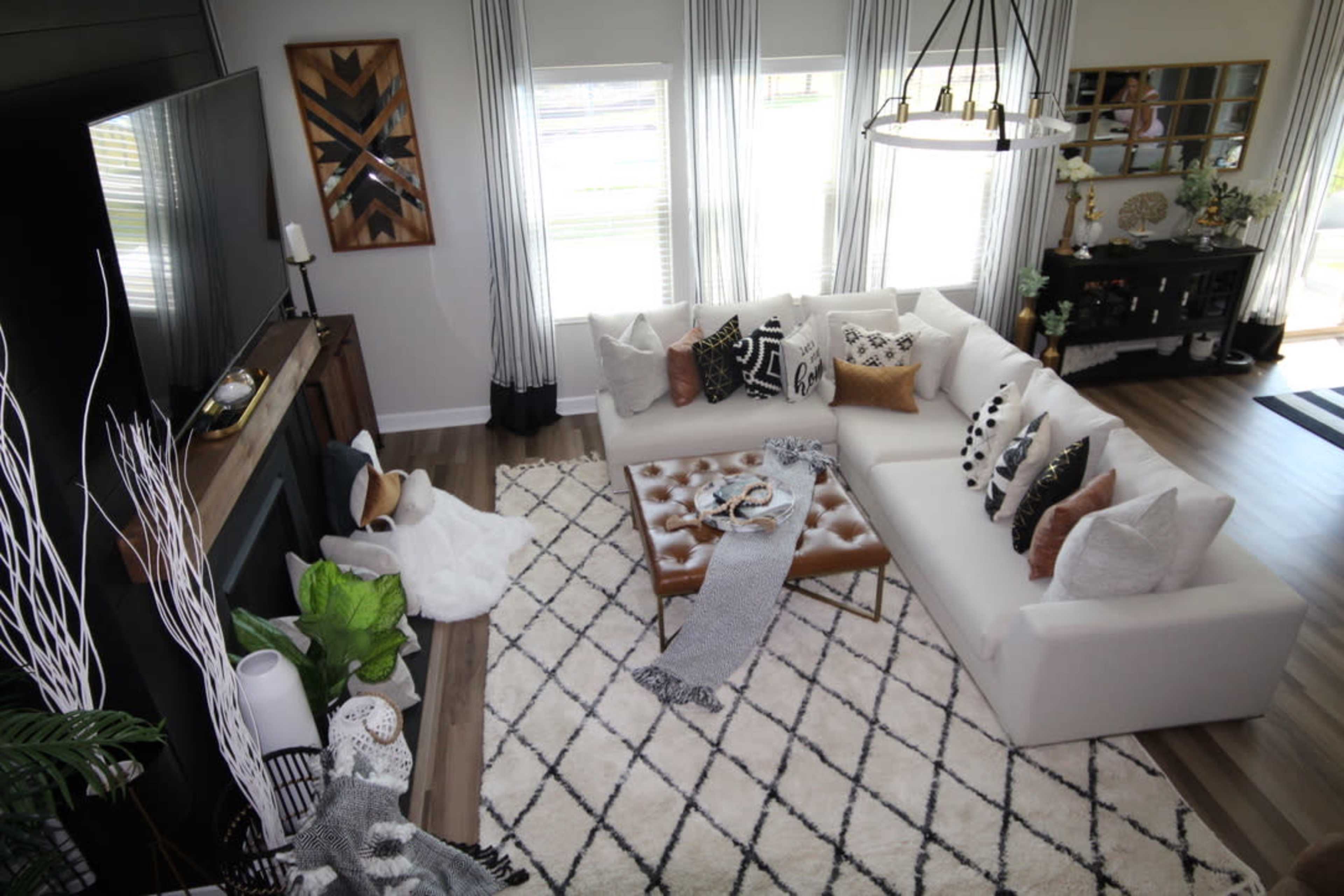 A modern living room featuring a large white sectional sofa, a coffee table with decorative items, and large windows with light gray curtains.