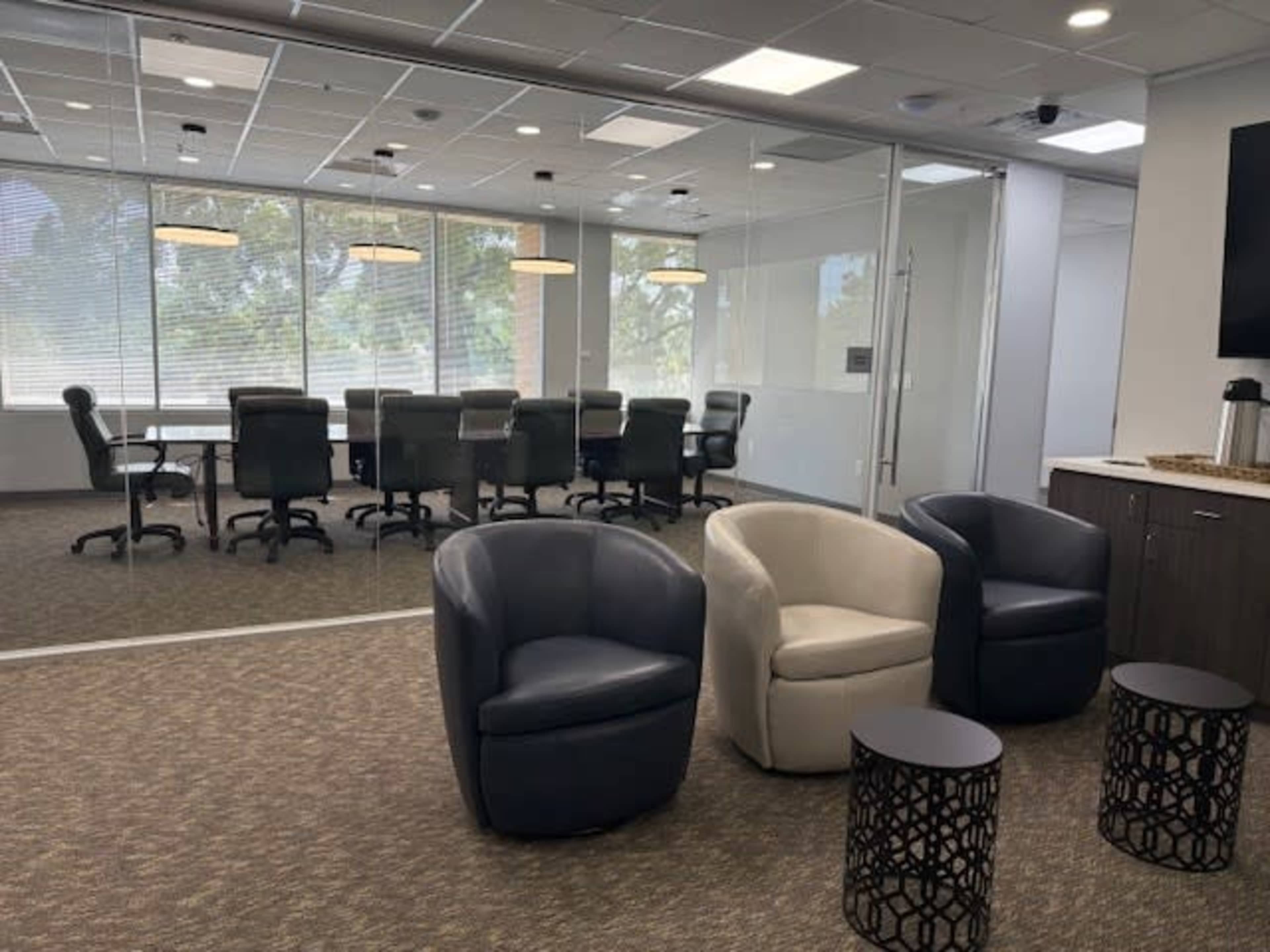 The image shows a modern office space with a conference room in the background and two armchairs along with side tables in the foreground.