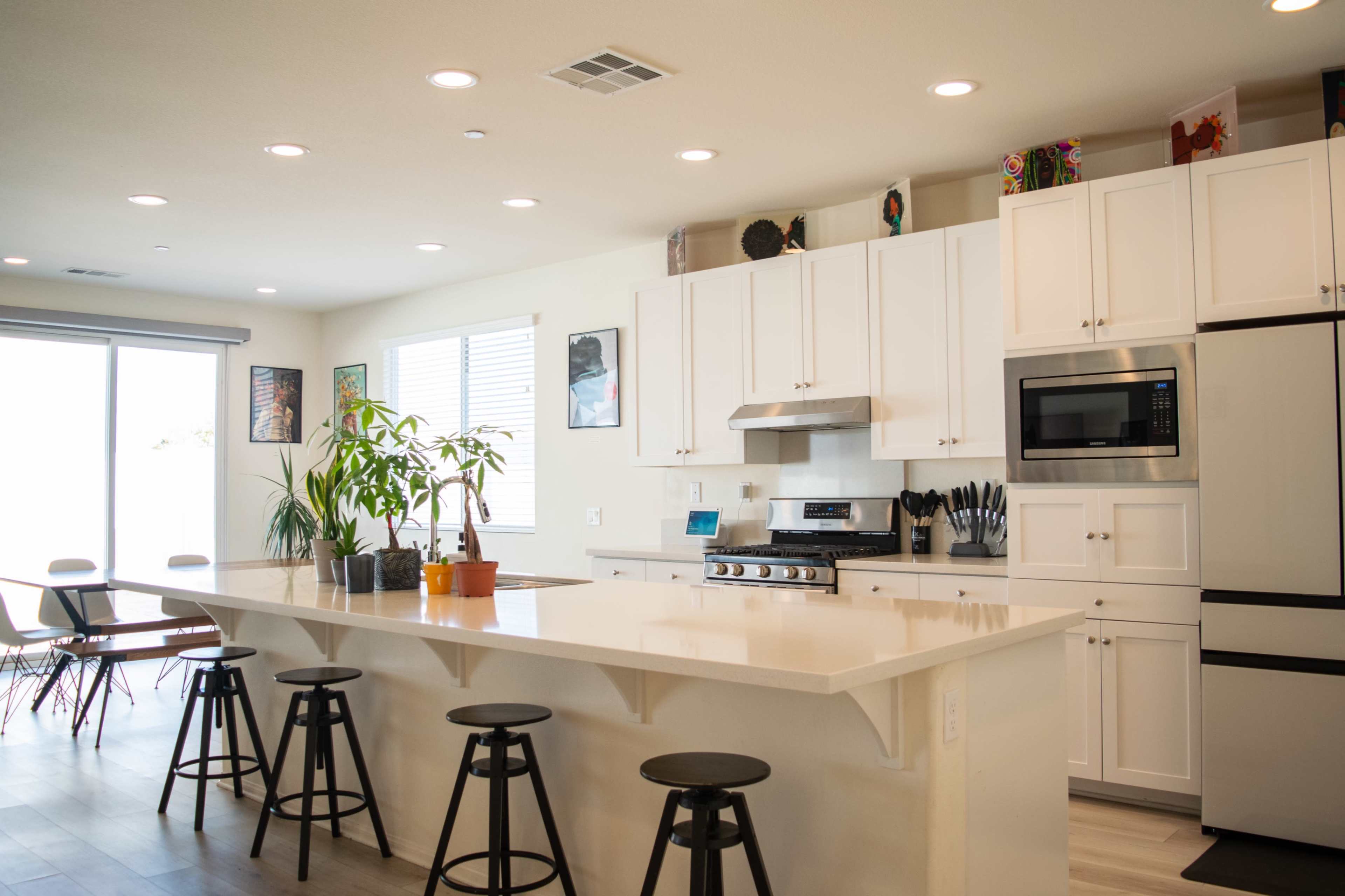 A modern kitchen features a central island with stools, white cabinetry, and stainless steel appliances.