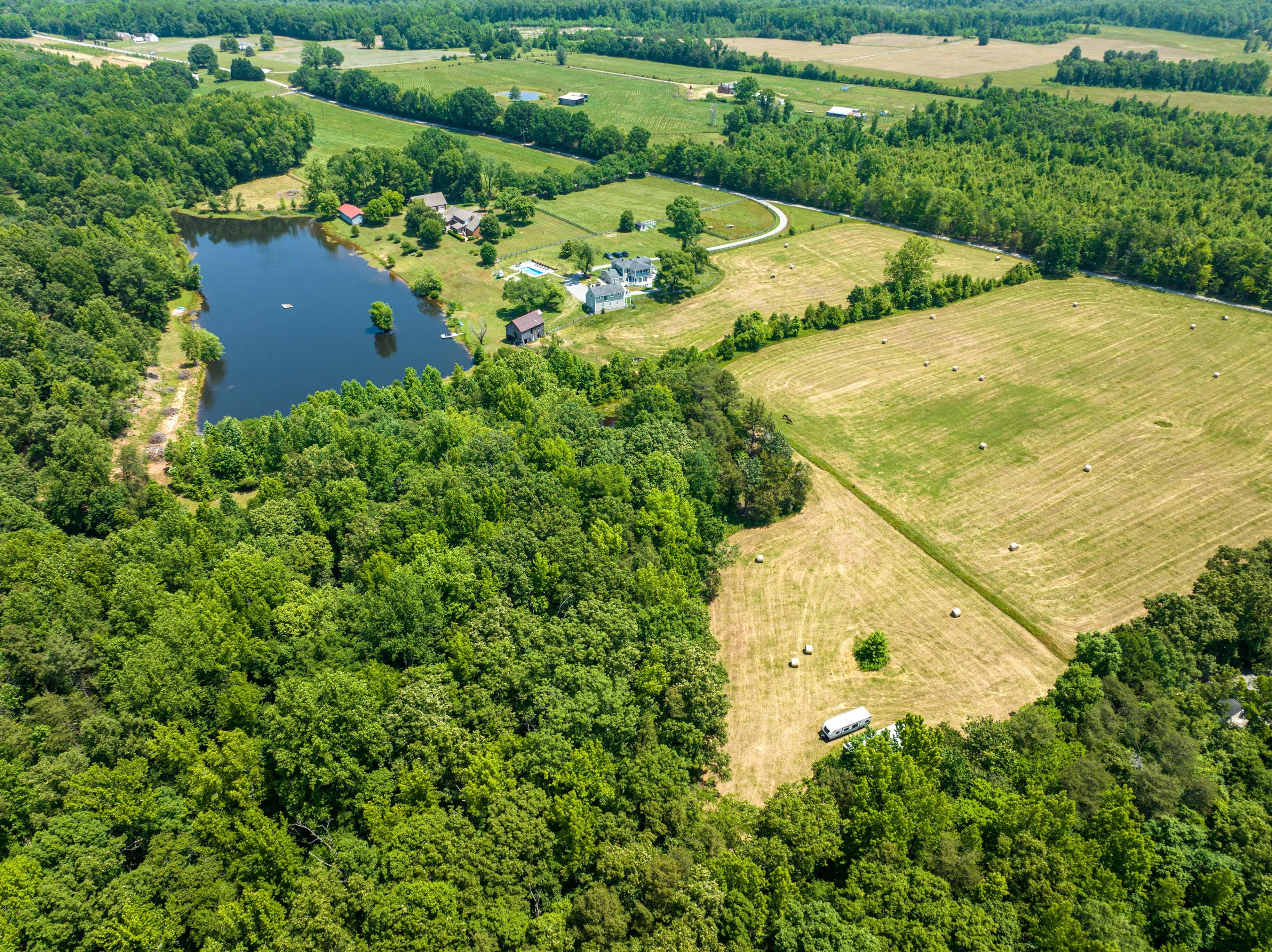 The image shows a rural landscape featuring a small pond surrounded by trees, with several fields and homes in the distance.