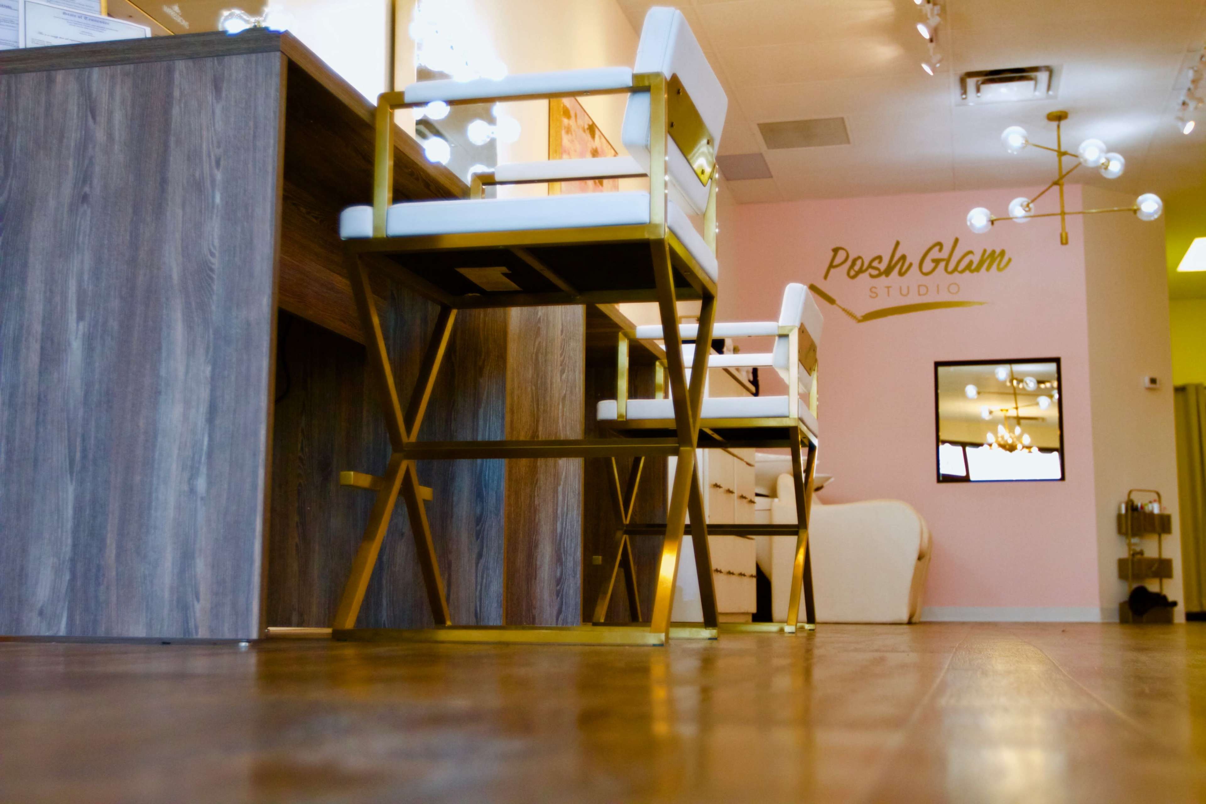The interior of a beauty studio featuring modern furniture, including white and gold chairs and a wooden reception desk.