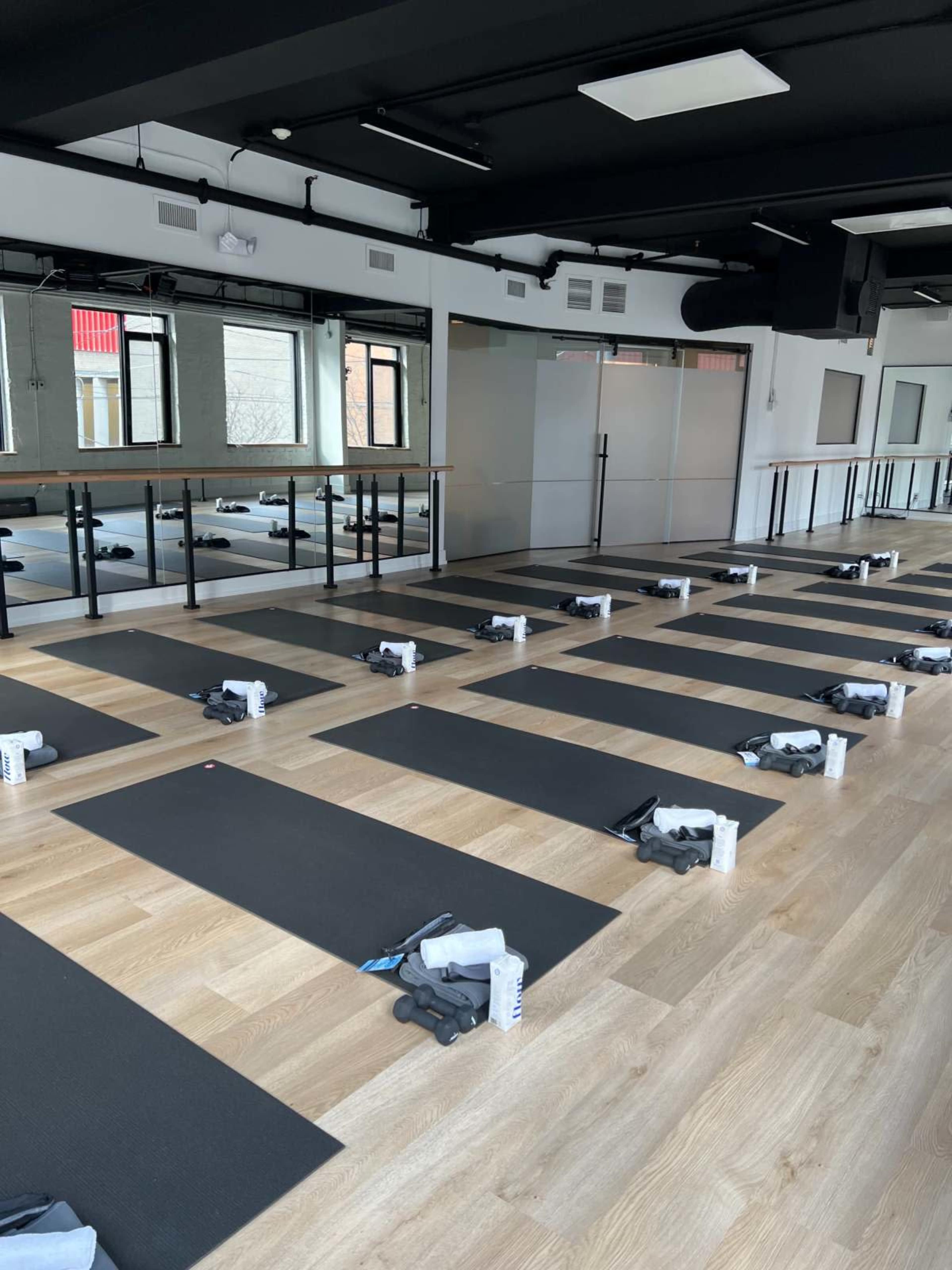 The image shows a yoga studio with neatly arranged mats and water bottles set up for a class.