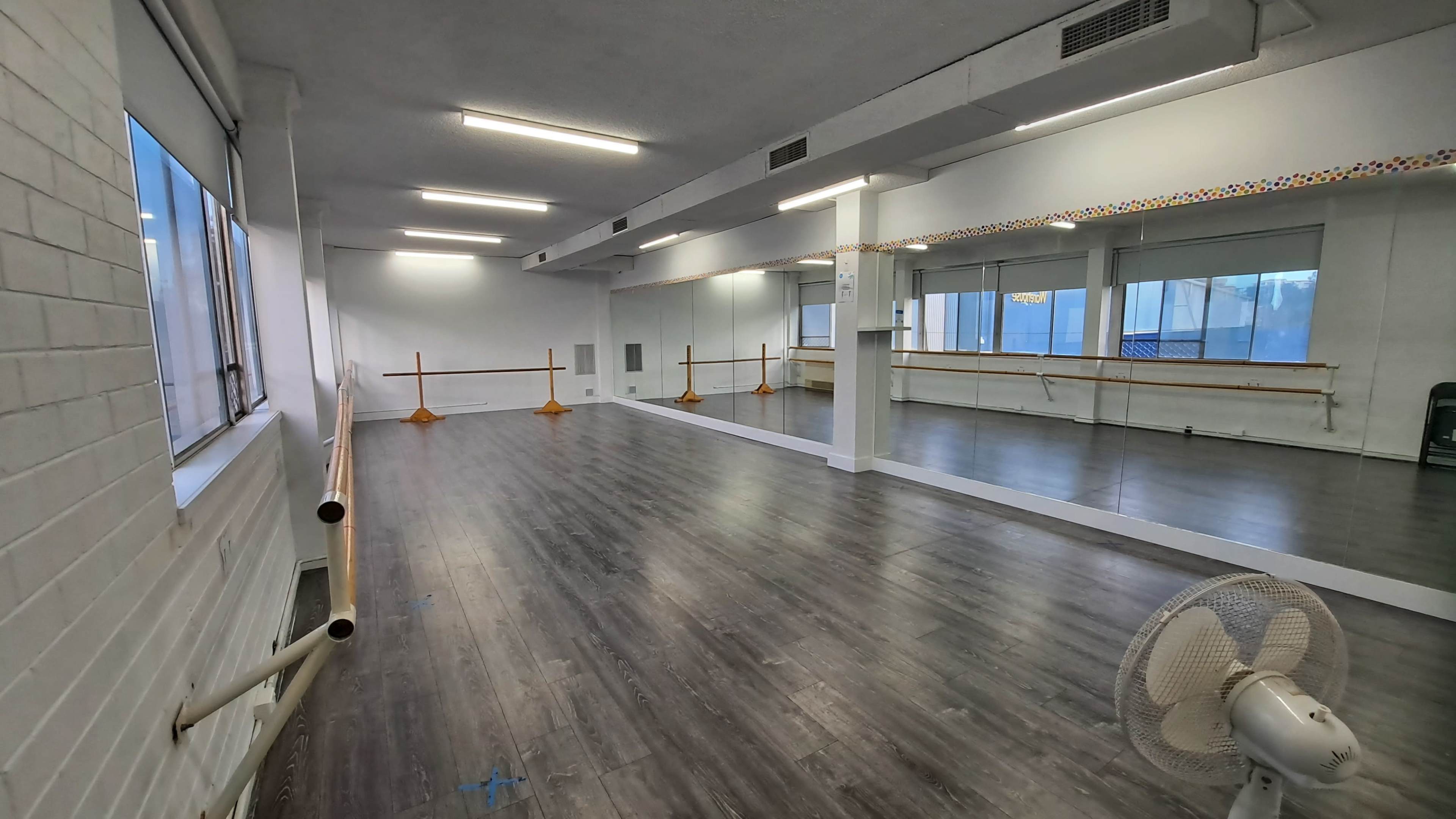 A spacious dance studio with mirrored walls, wooden flooring, and ballet barres along one side.