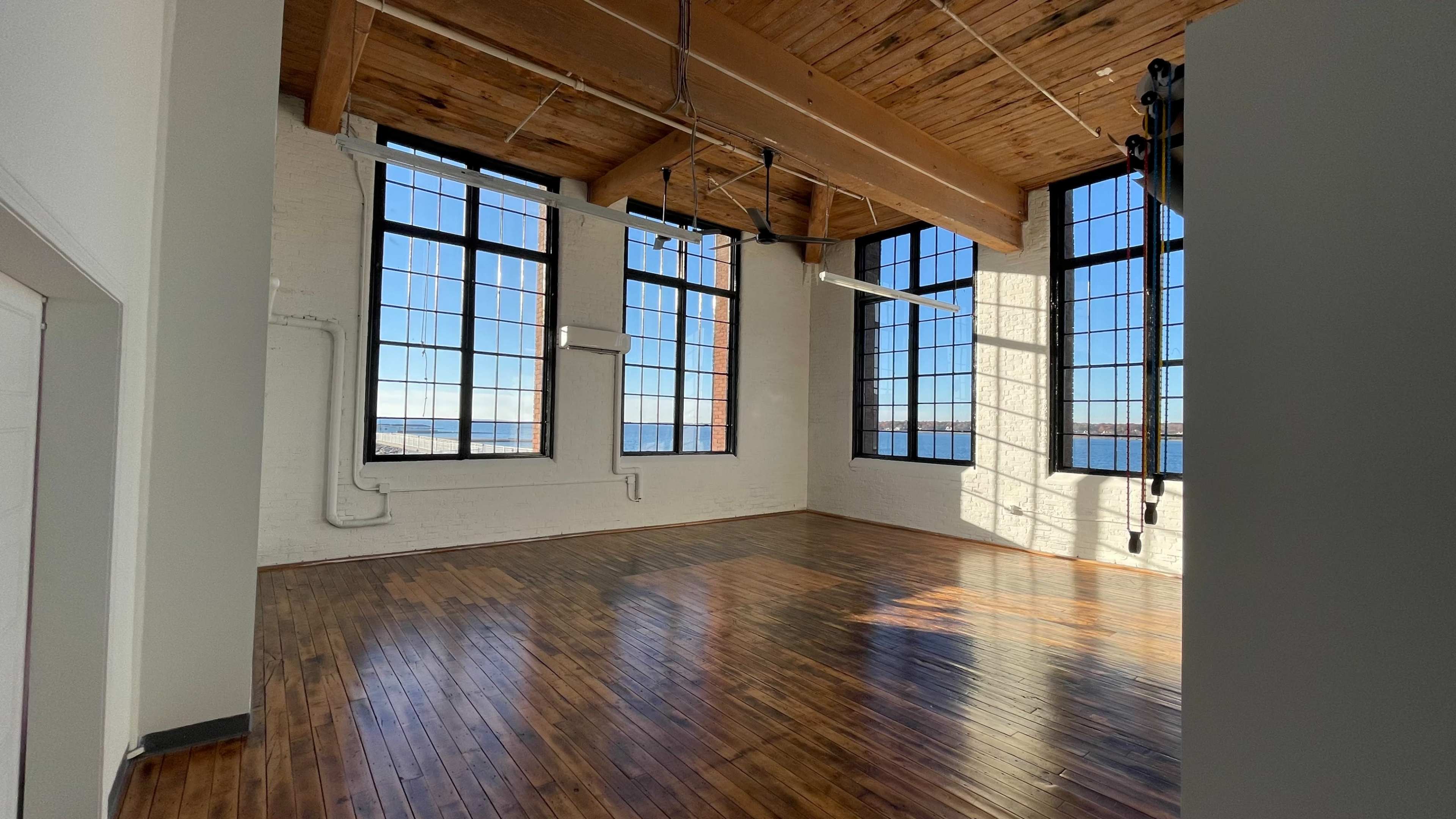 A spacious, well-lit room with large windows and polished wooden floors.