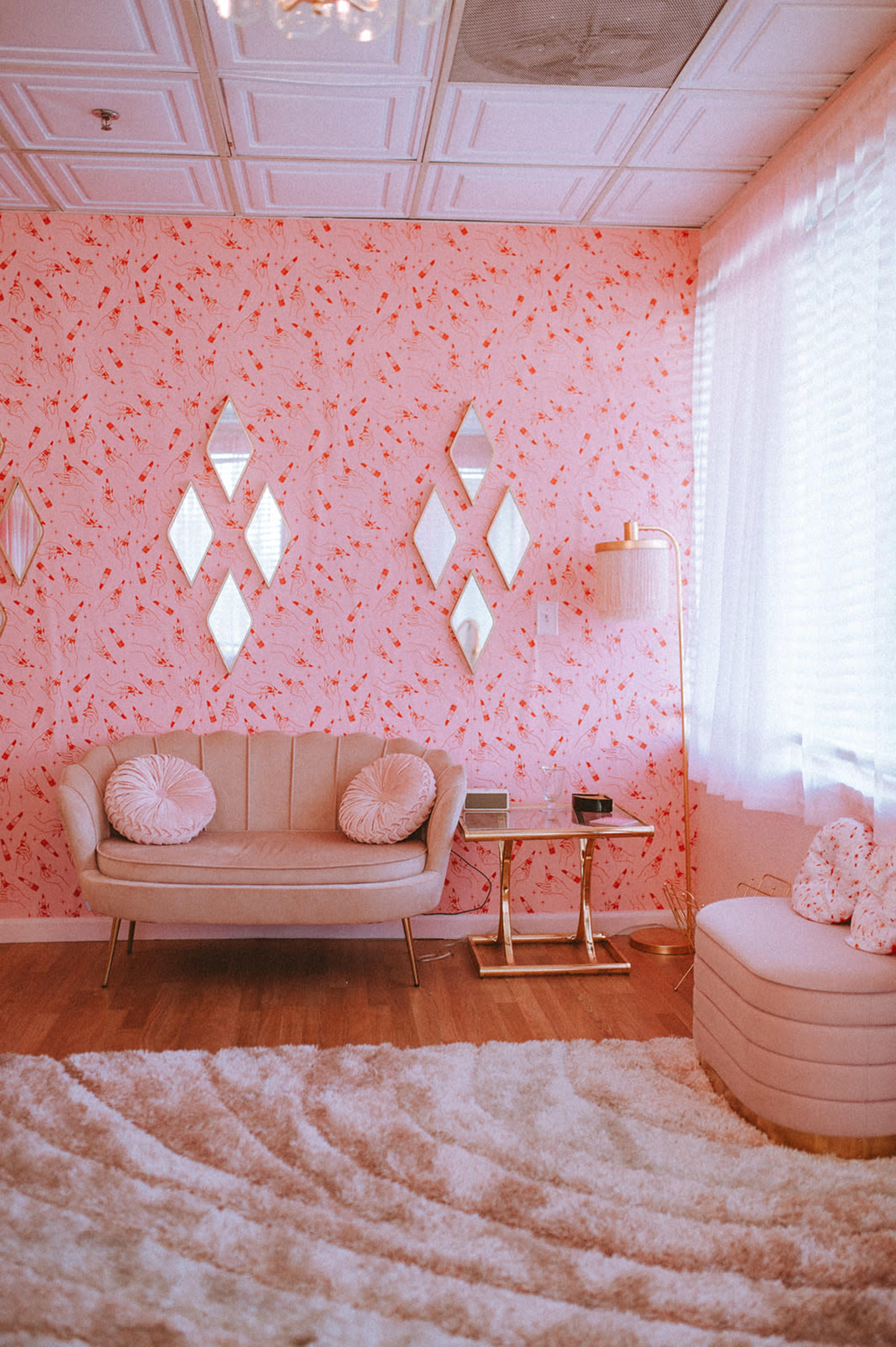 A cozy living room with a pink floral wallpaper, a light-colored sofa with round cushions, a small side table, and a fluffy white rug.