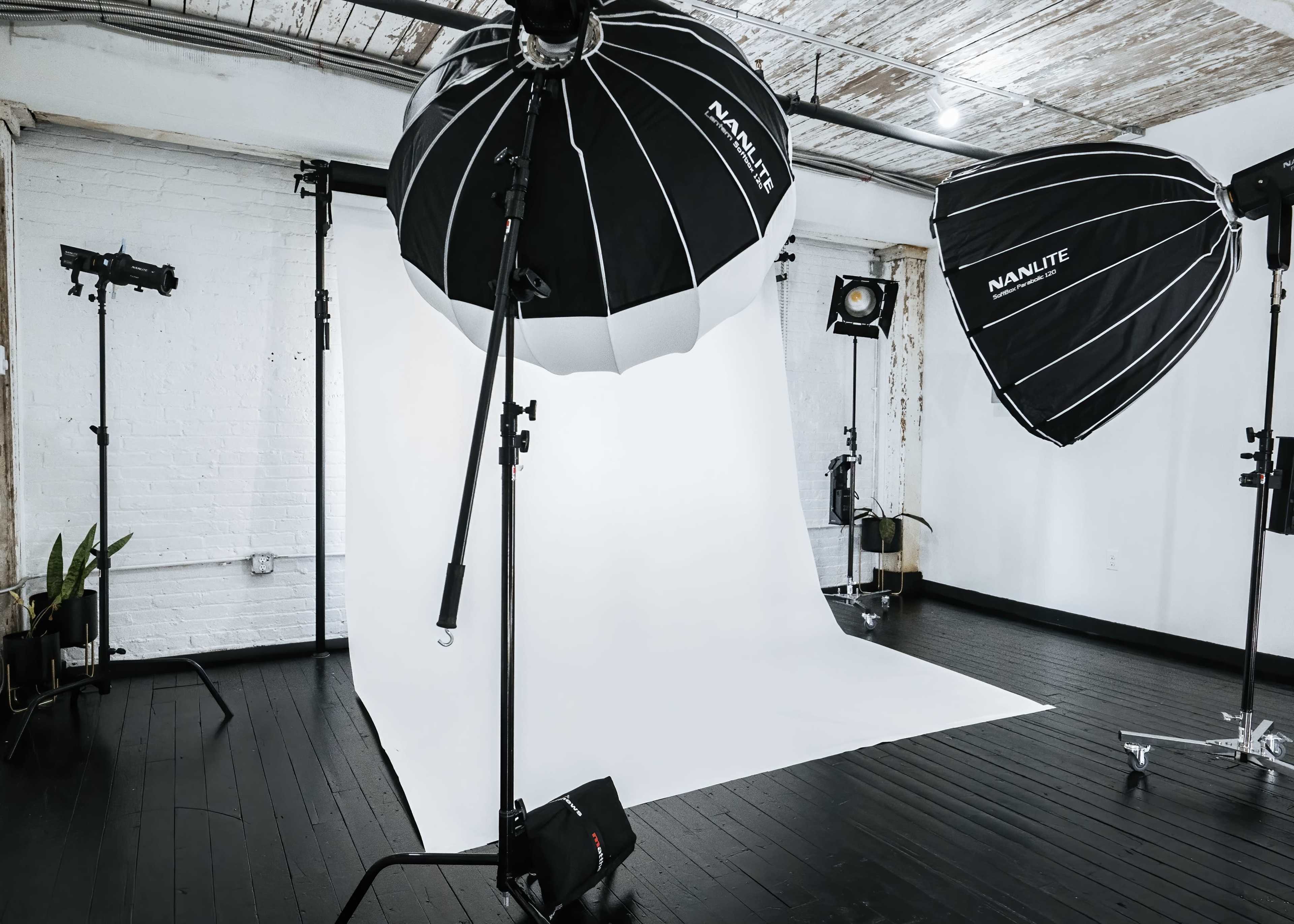 A photography studio equipped with two large softbox lights and a white backdrop, positioned on a dark wooden floor.