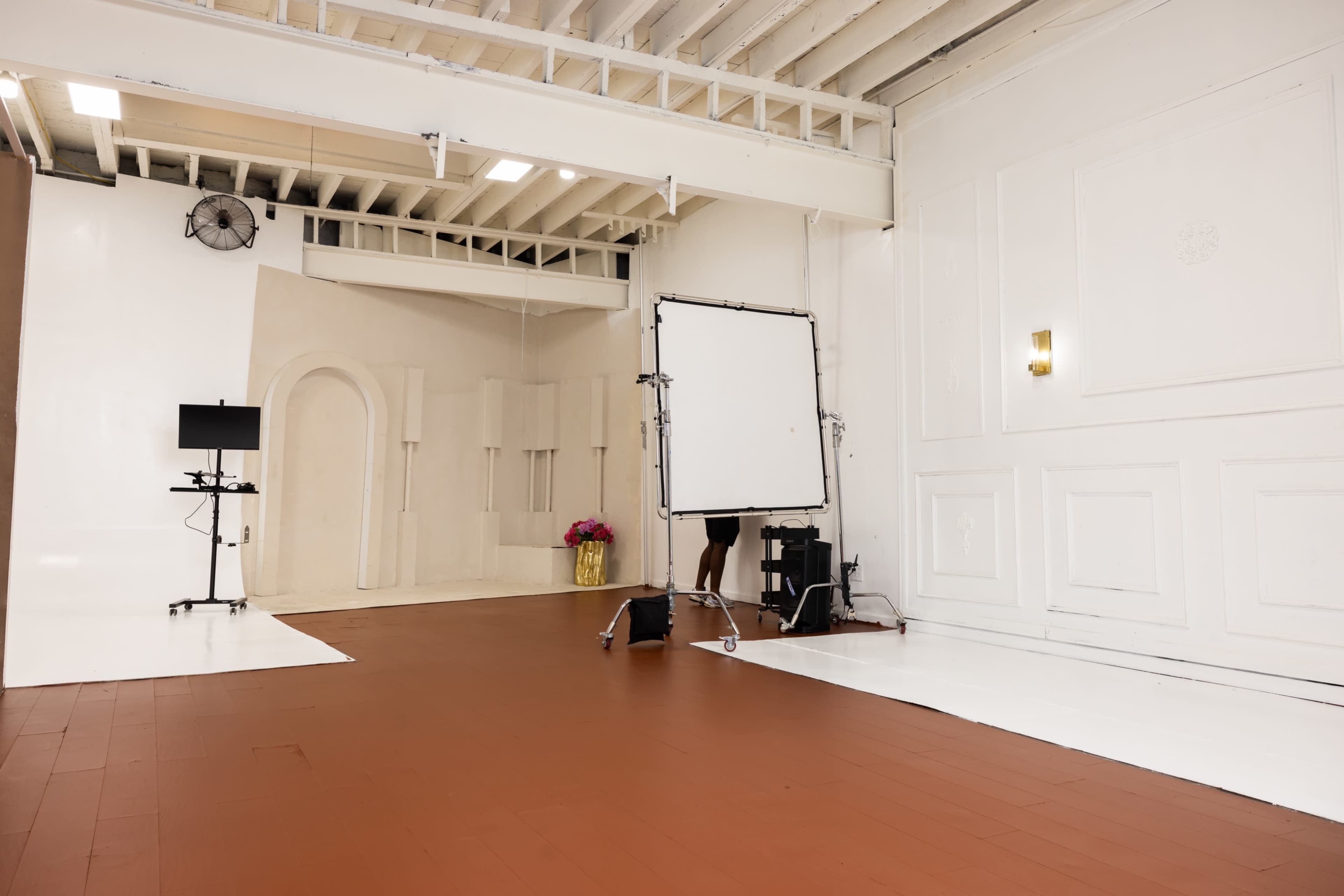 A spacious photography studio with a wooden floor, white walls, and various equipment arranged for a photoshoot.