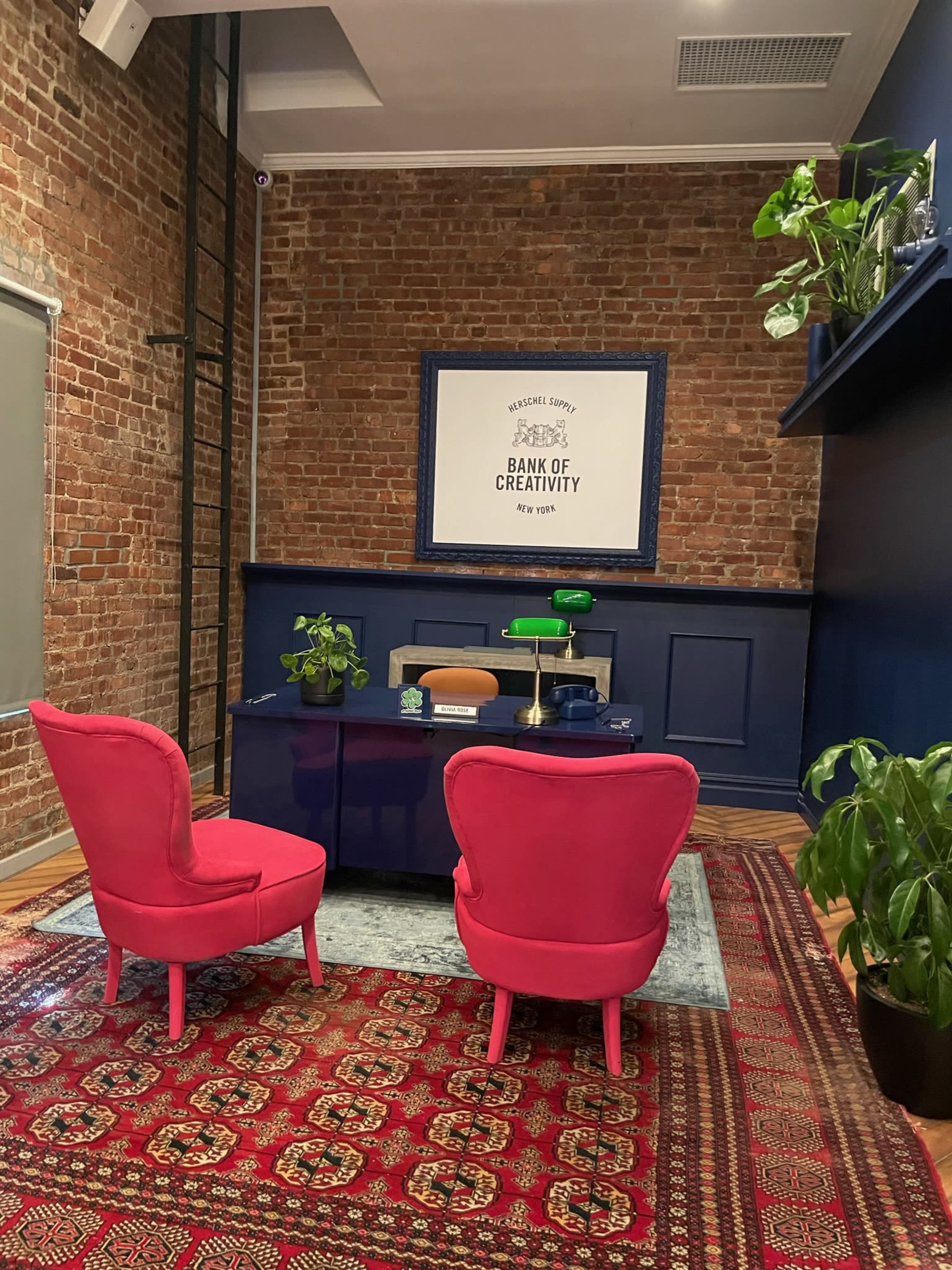 A cozy sitting area features two pink chairs facing a modern coffee table against a backdrop of exposed brick walls and dark blue accents.