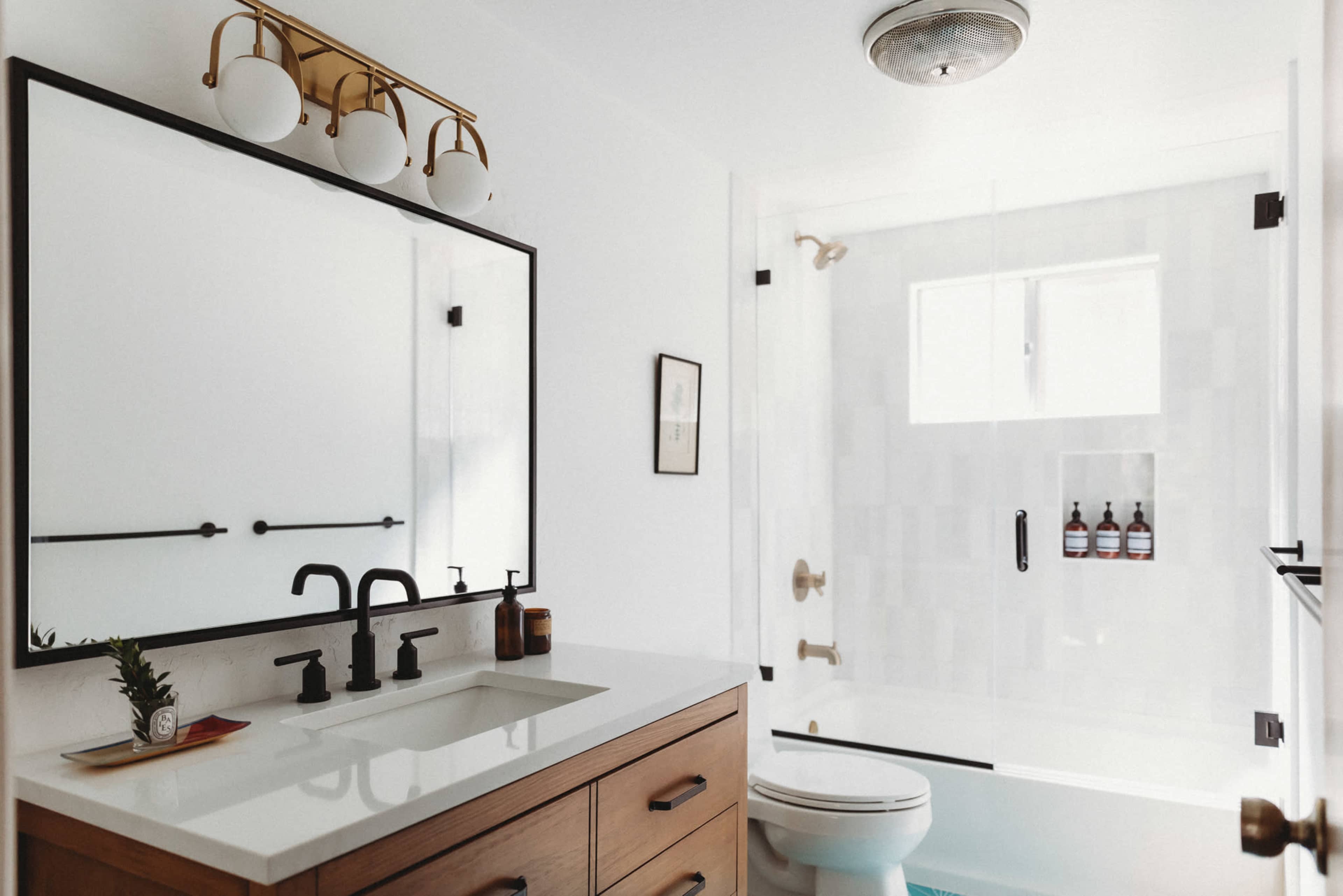 A modern bathroom featuring a wooden vanity with a rectangular sink, a large mirror, a glass-enclosed shower, and a toilet.