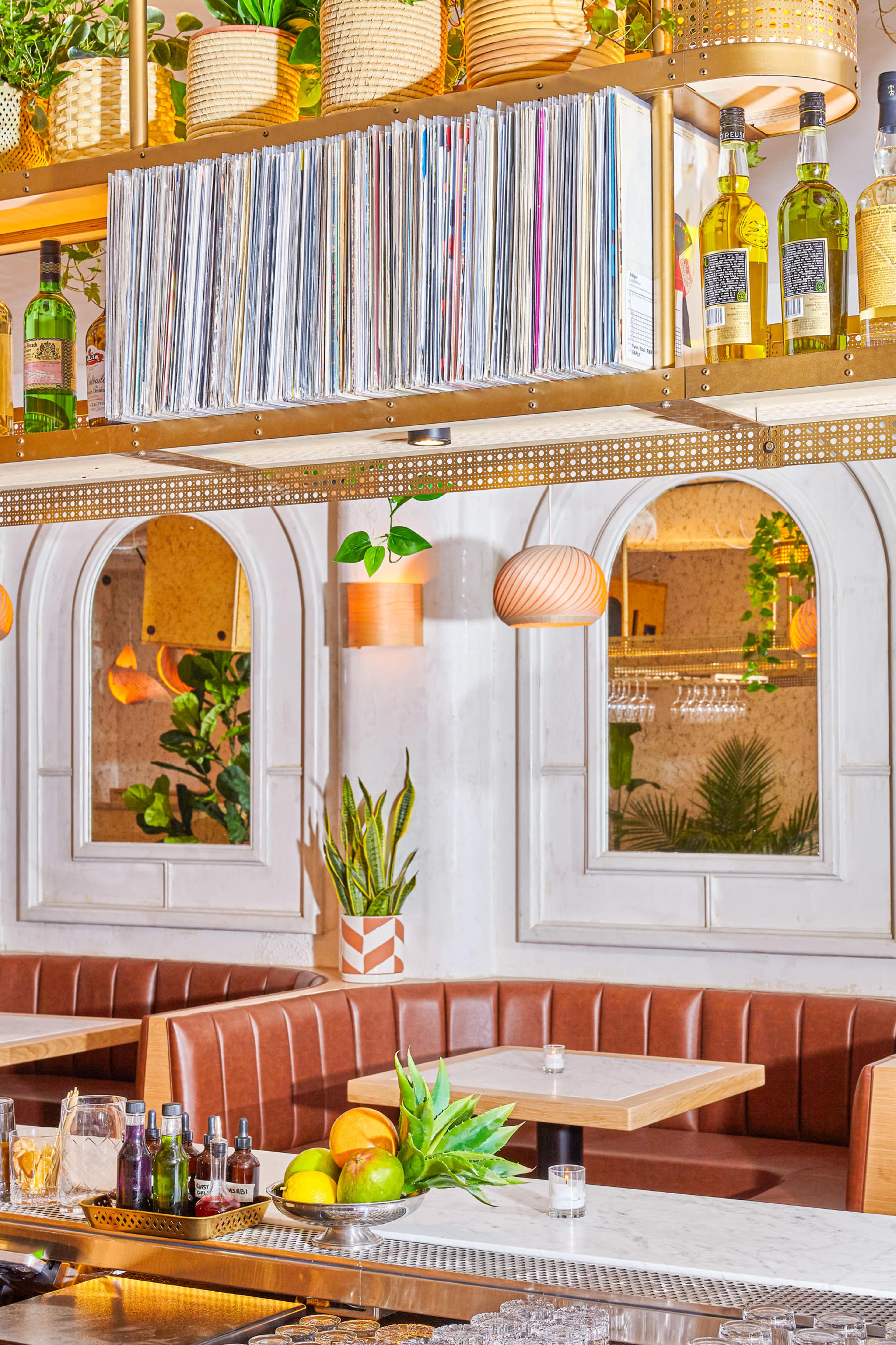 A restaurant interior featuring brown leather booths, a bar with various condiments, and shelves displaying wine bottles and vinyl records above.