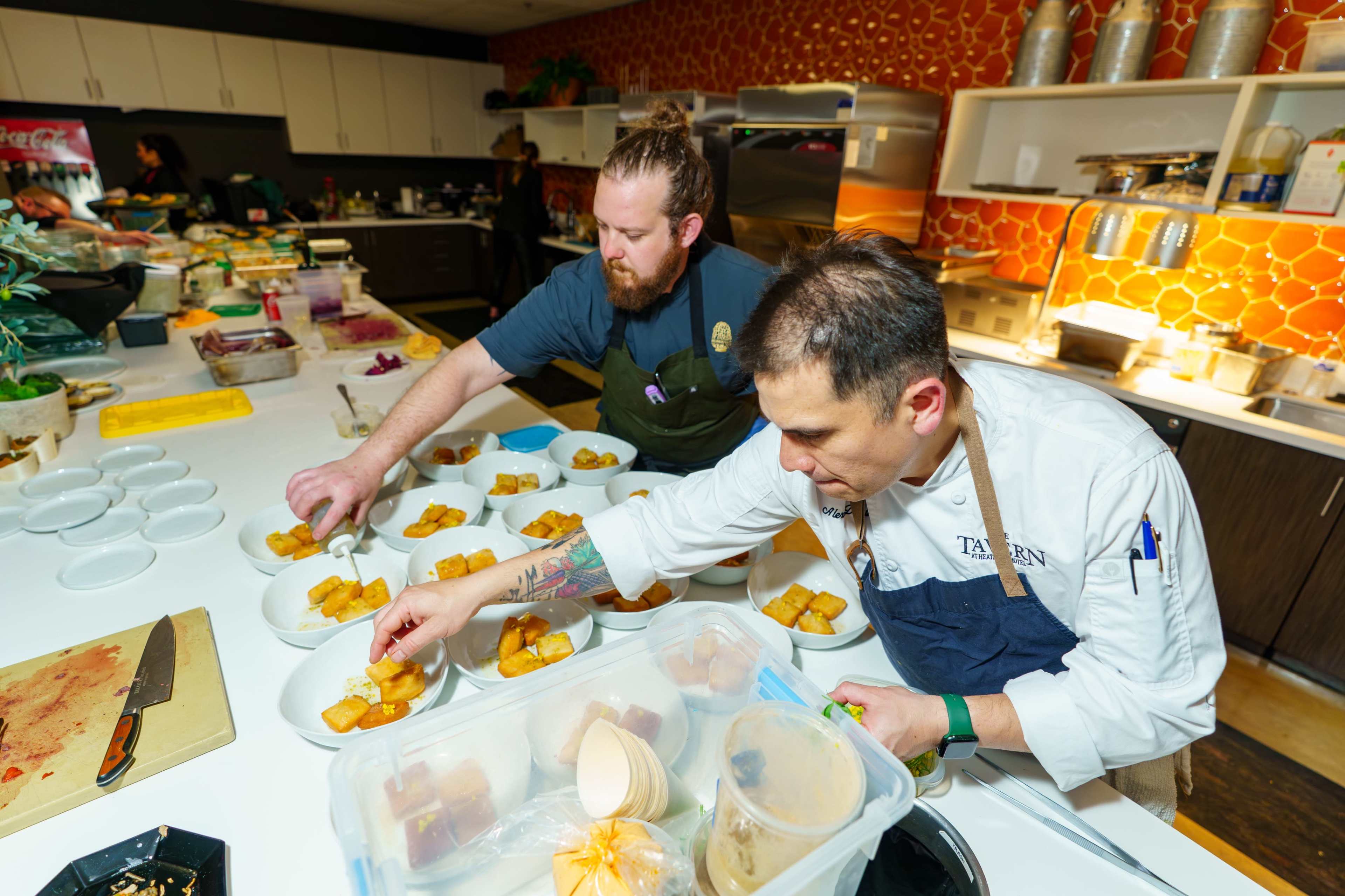 Two chefs are meticulously plating individual servings of dessert in a busy kitchen.