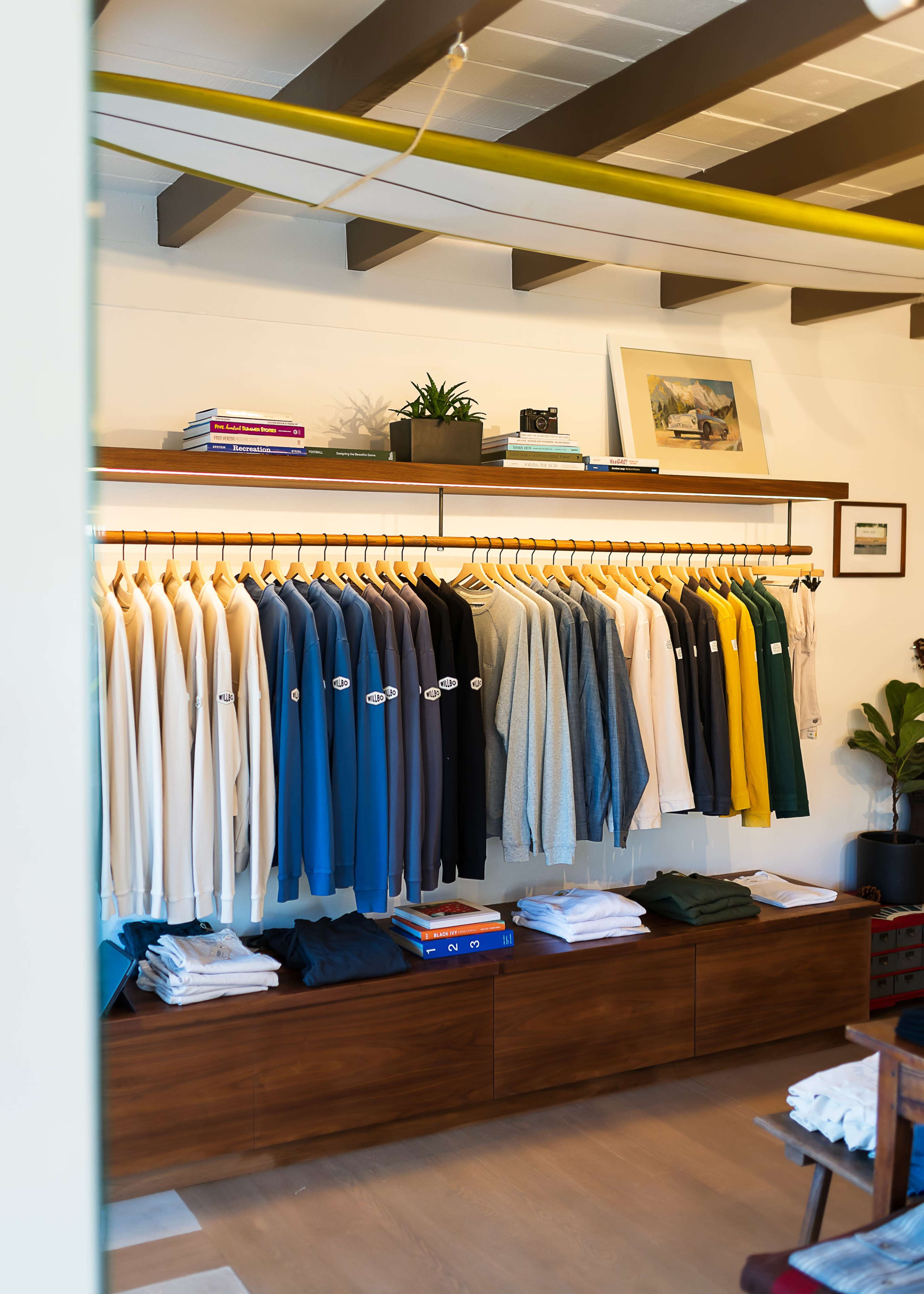 A neatly organized clothing display showcases various sweaters hanging on a wooden rack, with additional folded garments on a low dresser beneath.