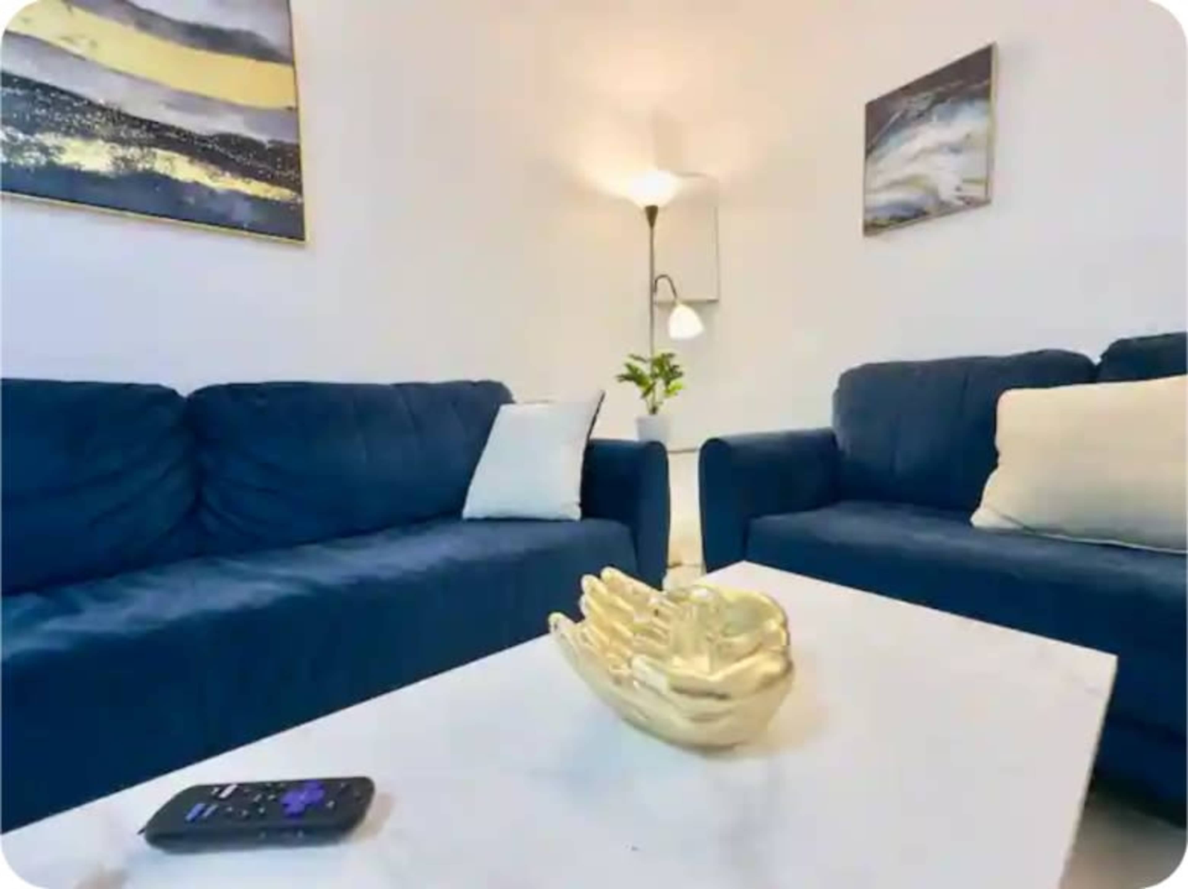 The image shows a modern living room with two blue sofas facing each other, a white coffee table, and a decorative piece on the table.