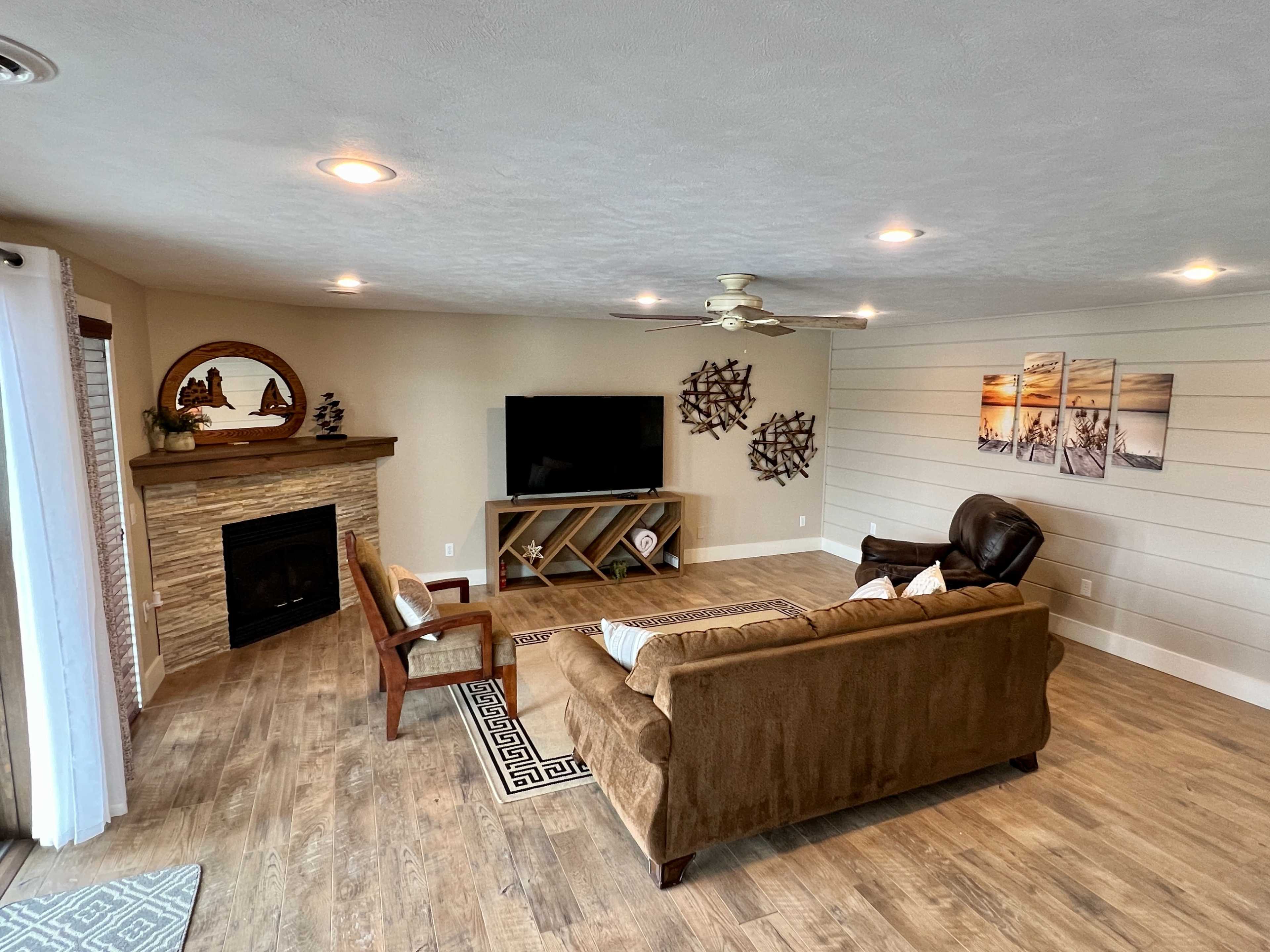 The image shows a living room with a brown couch, a television on a stand, a fireplace, and decor on the walls.
