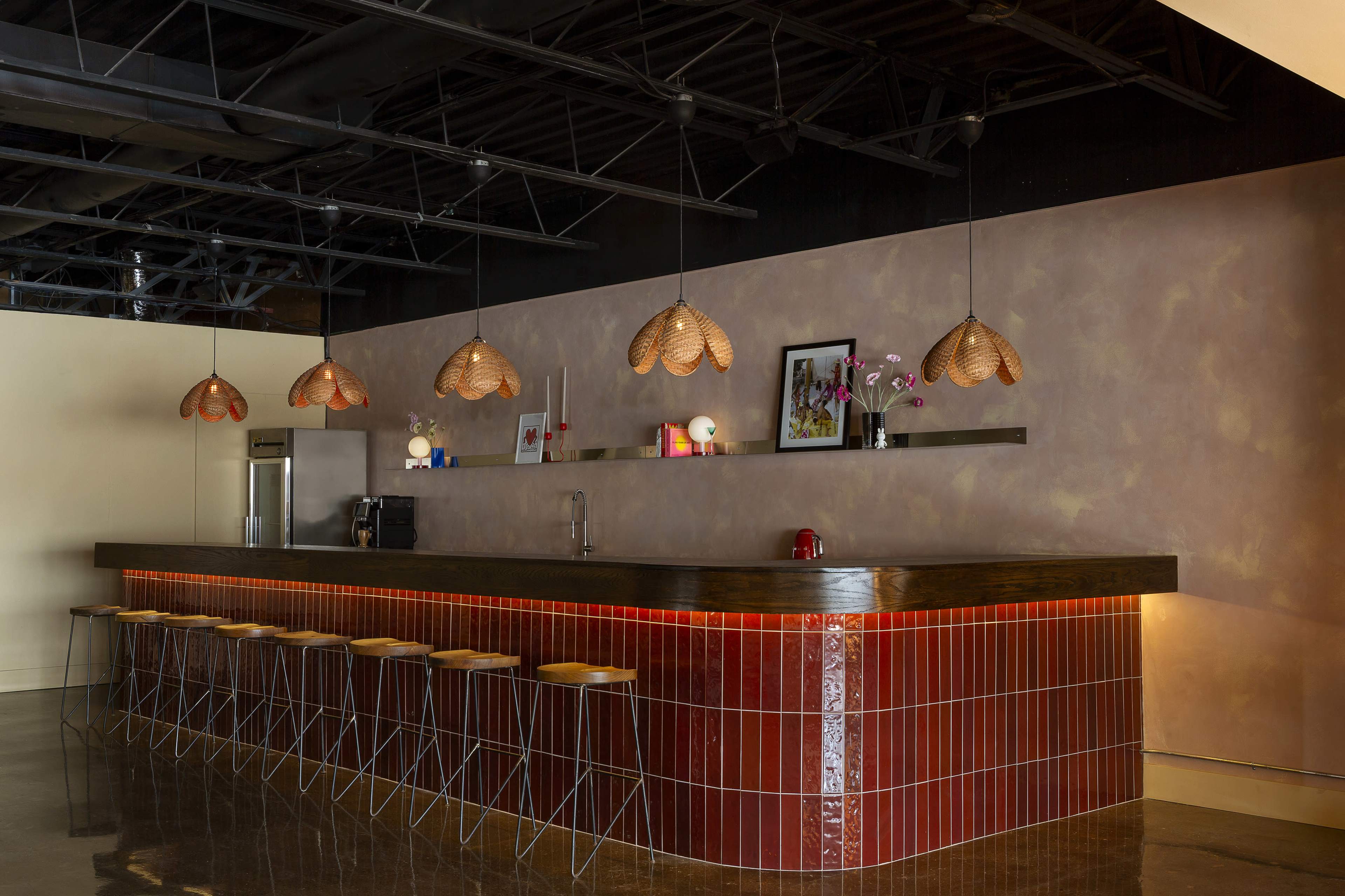The image features a modern bar area with a long wooden counter, bar stools, and pendant lights hanging from the ceiling.