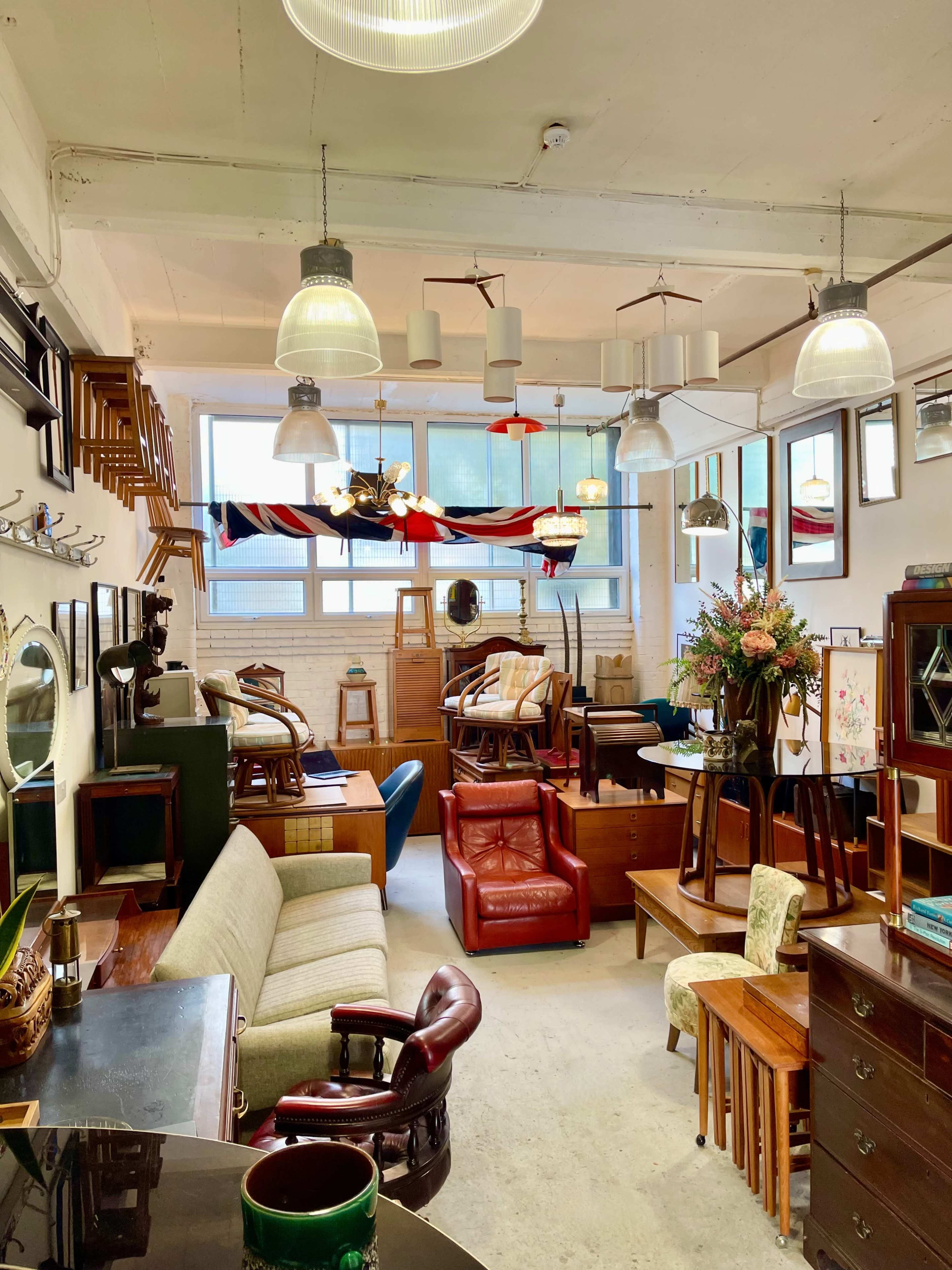 A spacious interior filled with various pieces of furniture, including chairs, tables, and shelving, under bright industrial lighting.