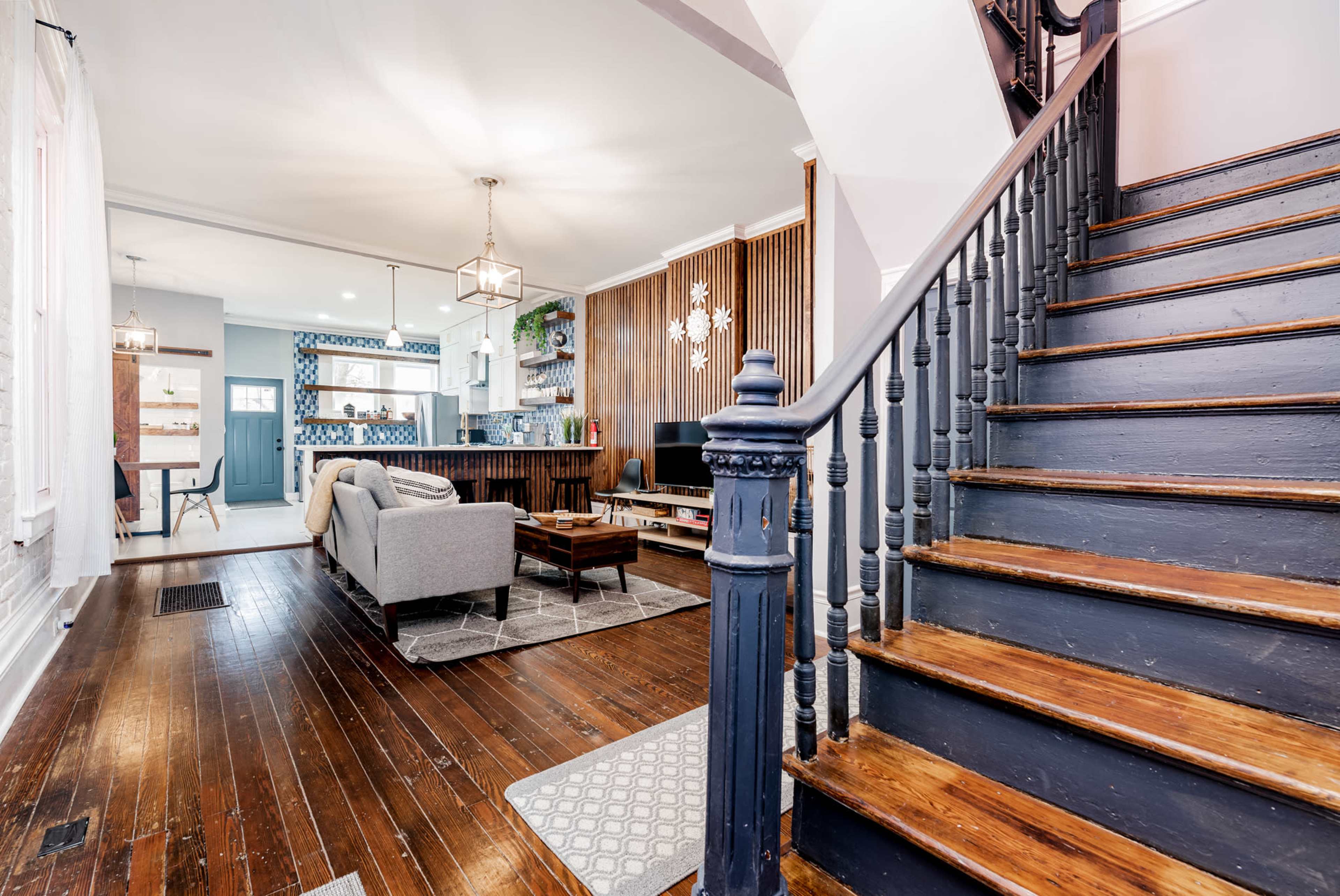 A wooden staircase leads to an open living area with a sofa, coffee table, and various decorations.