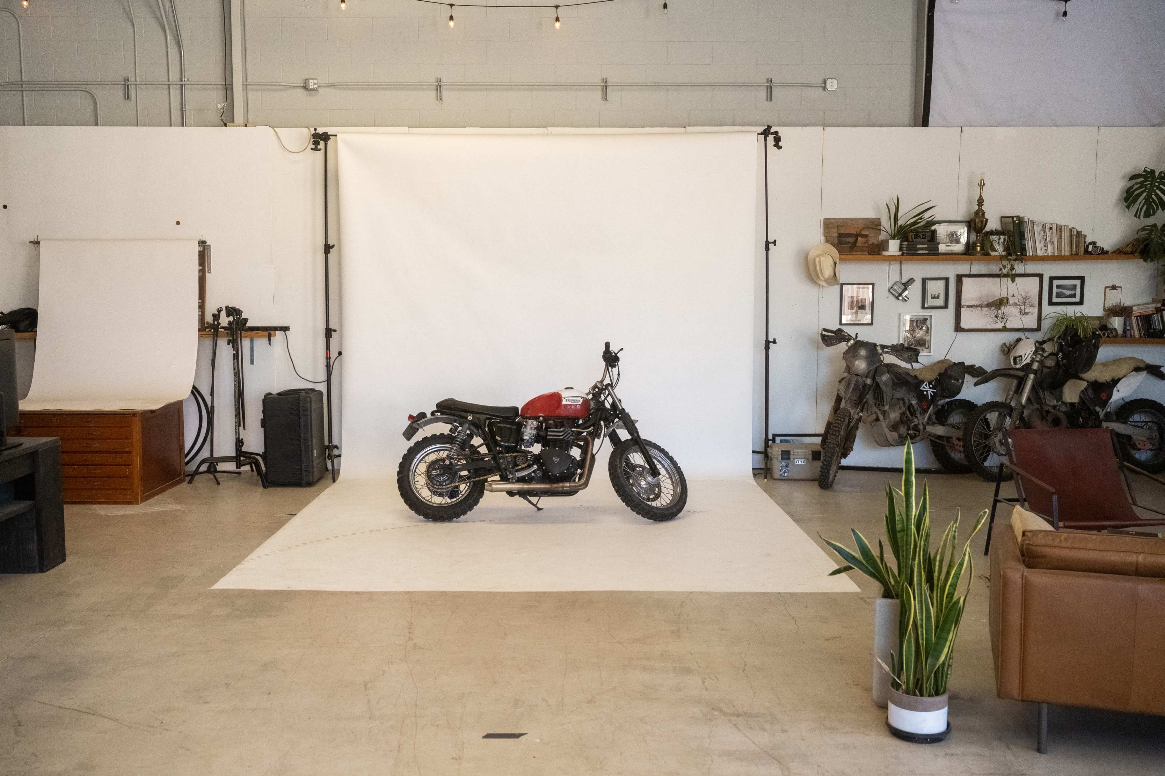 A motorcycle is positioned on a white backdrop in a spacious studio with various props and decor around the perimeter.