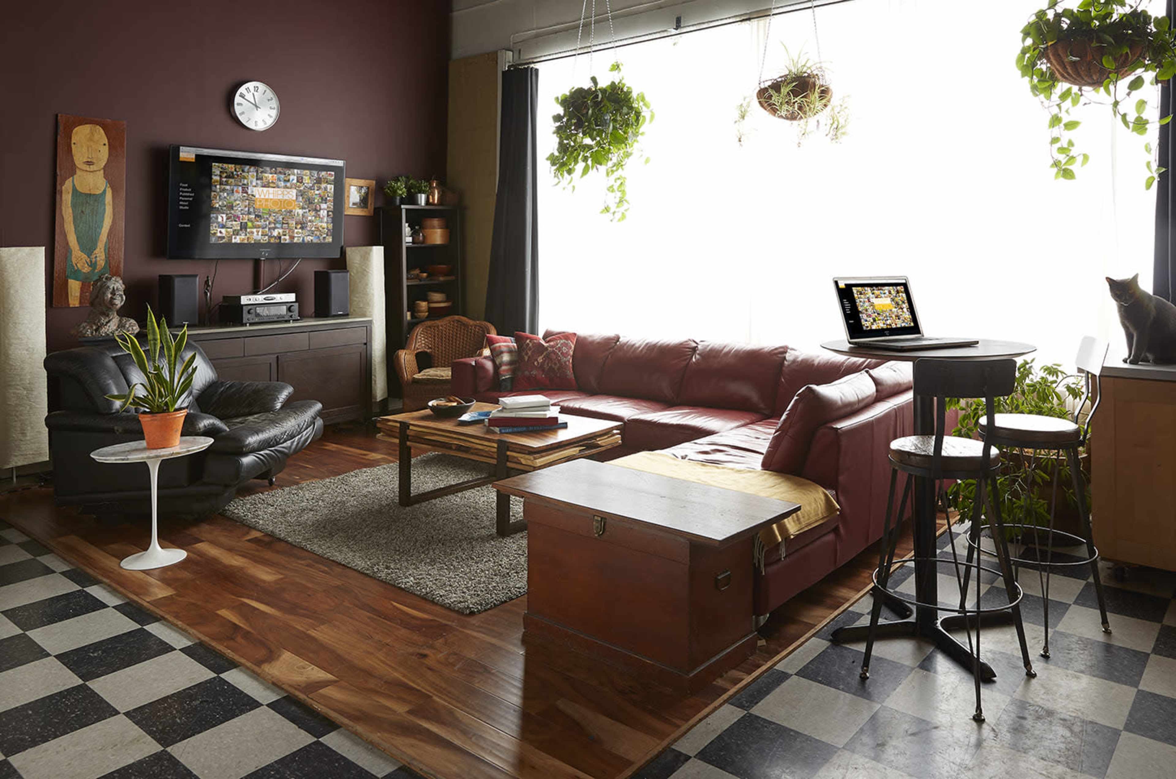 The image depicts a cozy living room with a red sectional sofa, a wooden coffee table, a large window with hanging plants, and a black and white checkered floor.