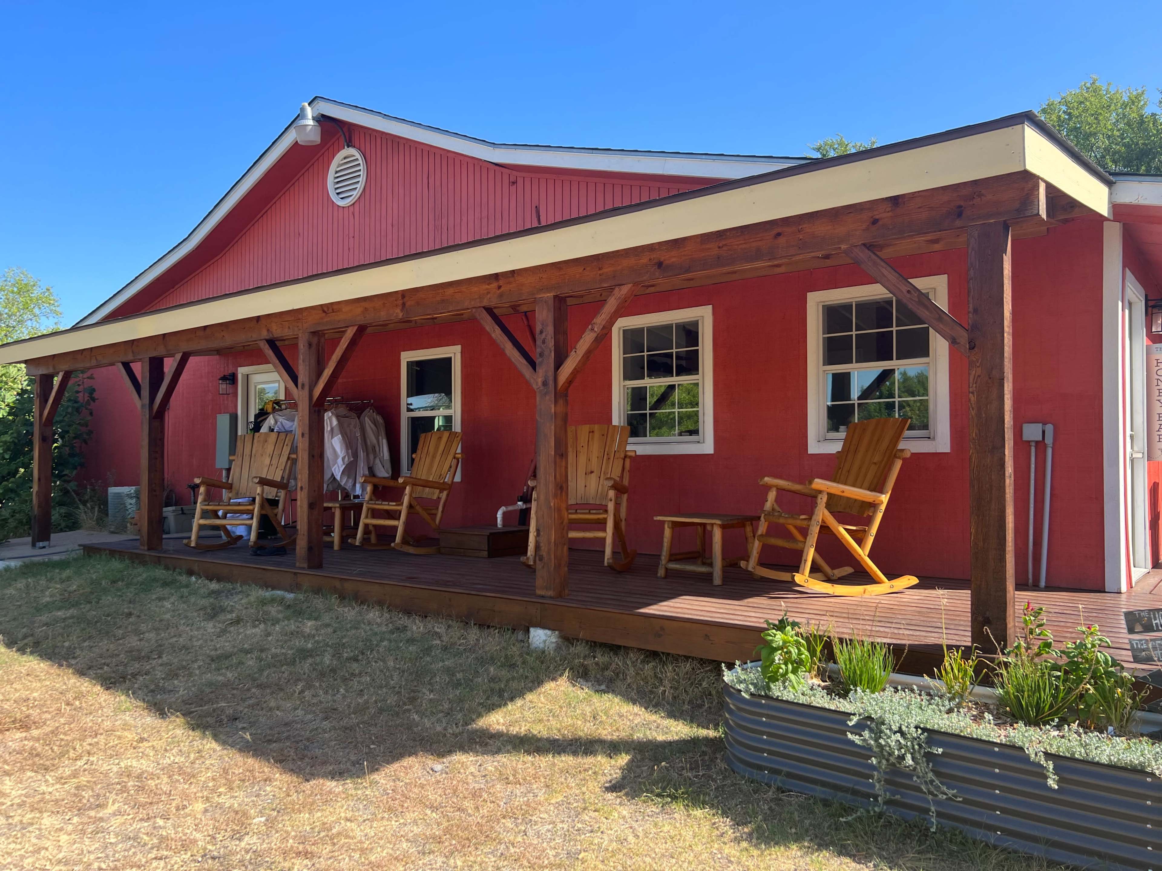 A red house with a covered porch features several wooden rocking chairs and a few plants in a garden bed.