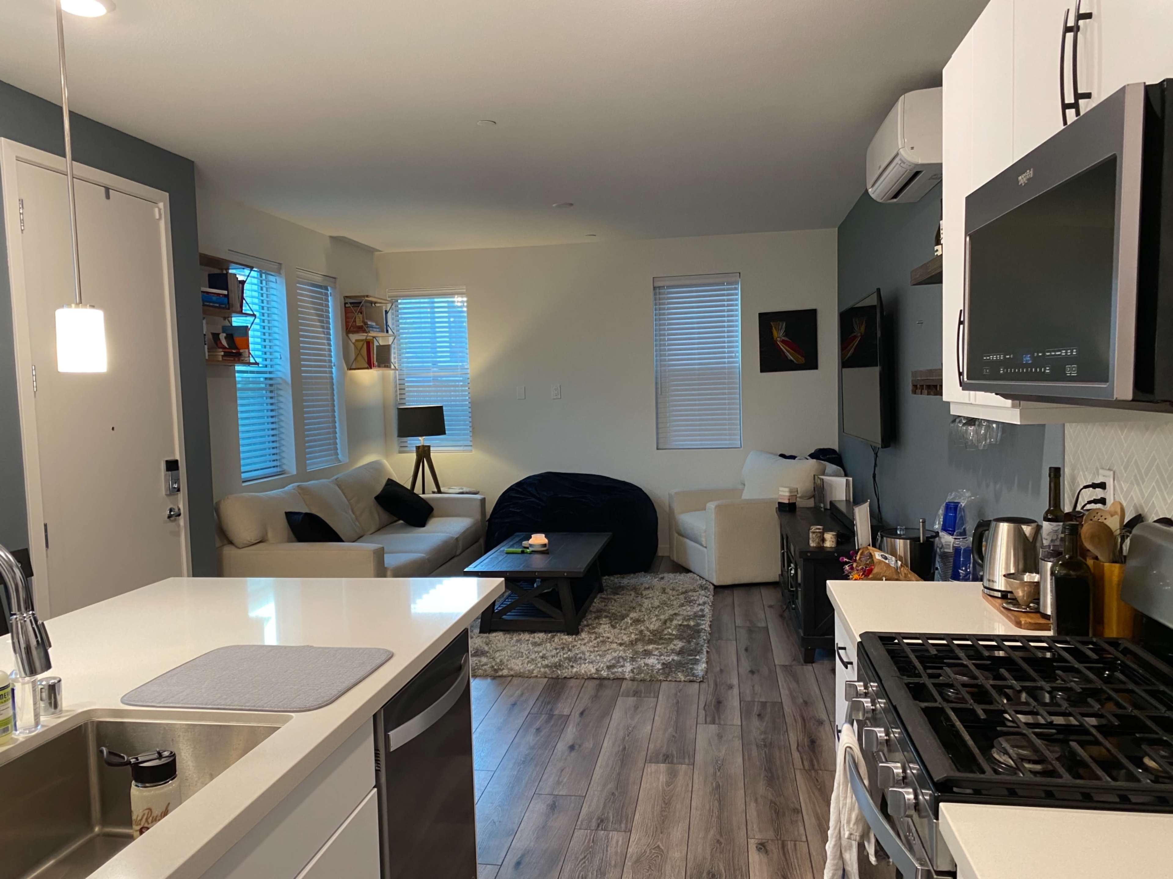 A modern kitchen and living area featuring white cabinetry, a gas stove, a seating area with a light sofa, and a dark coffee table.