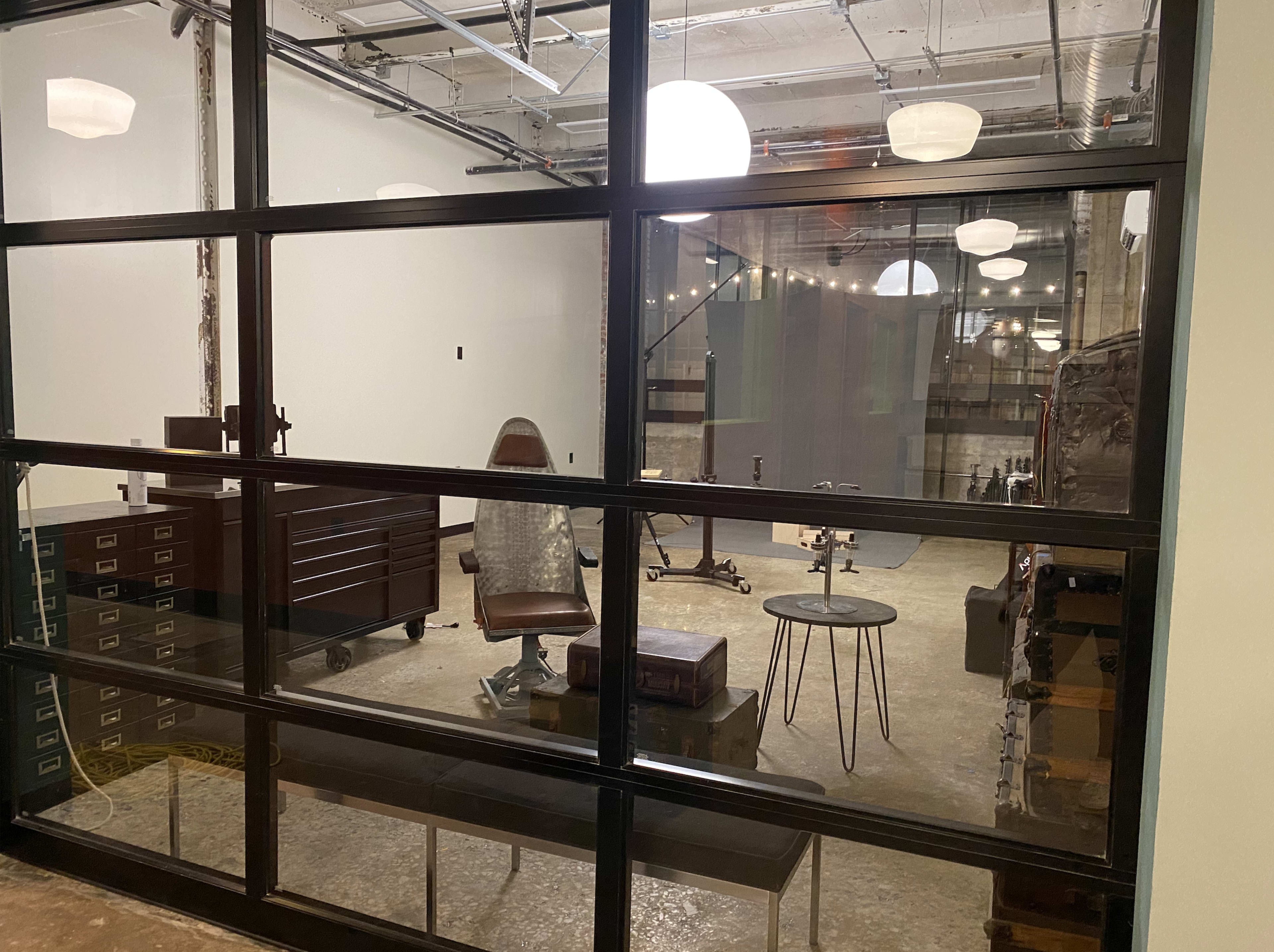 A modern office space with a leather chair, a desk, and wall-mounted fixtures visible through a large glass window.