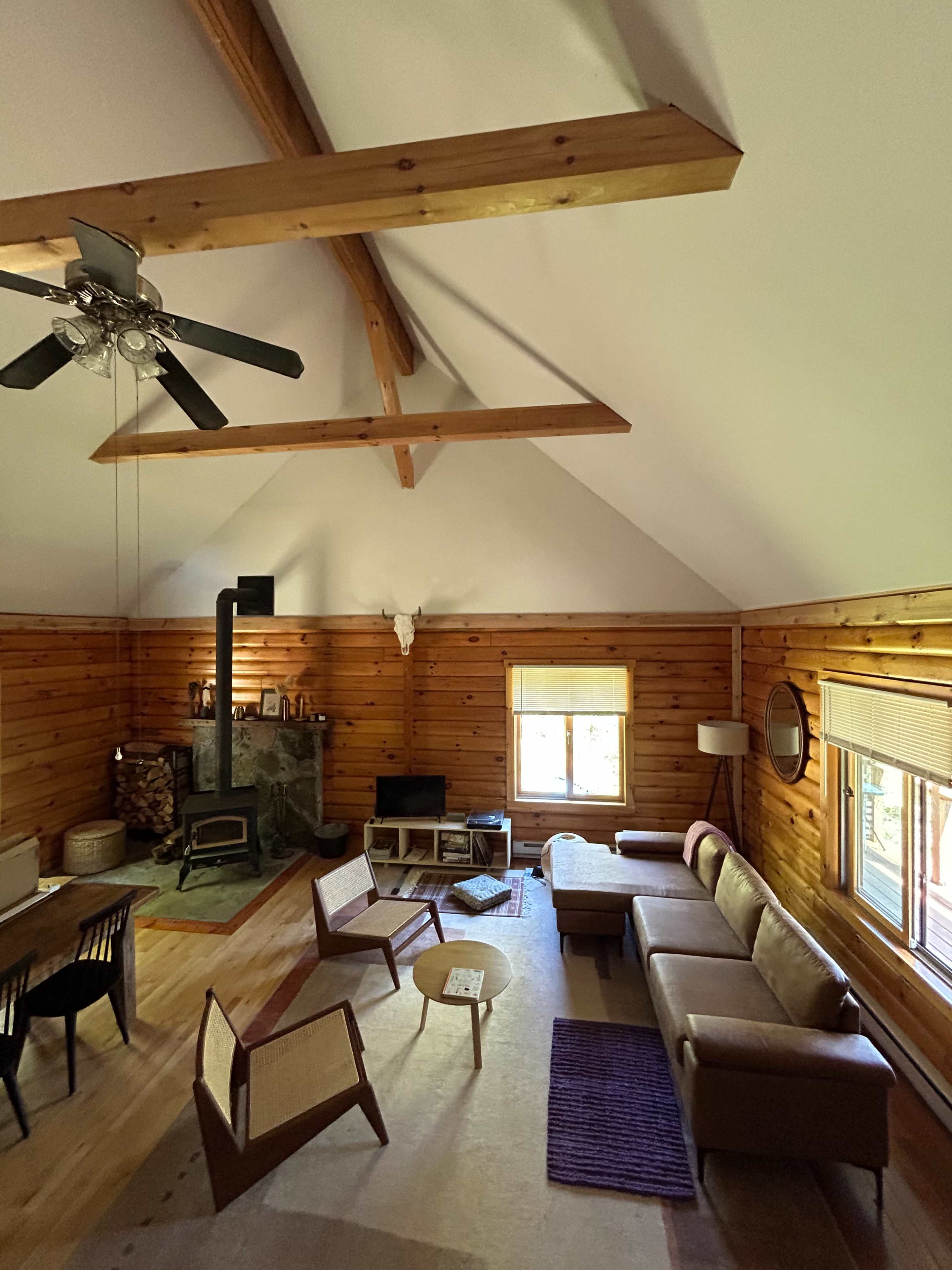 The image shows a cozy wooden living room with high ceilings, a fireplace, and a mix of modern and rustic furniture.