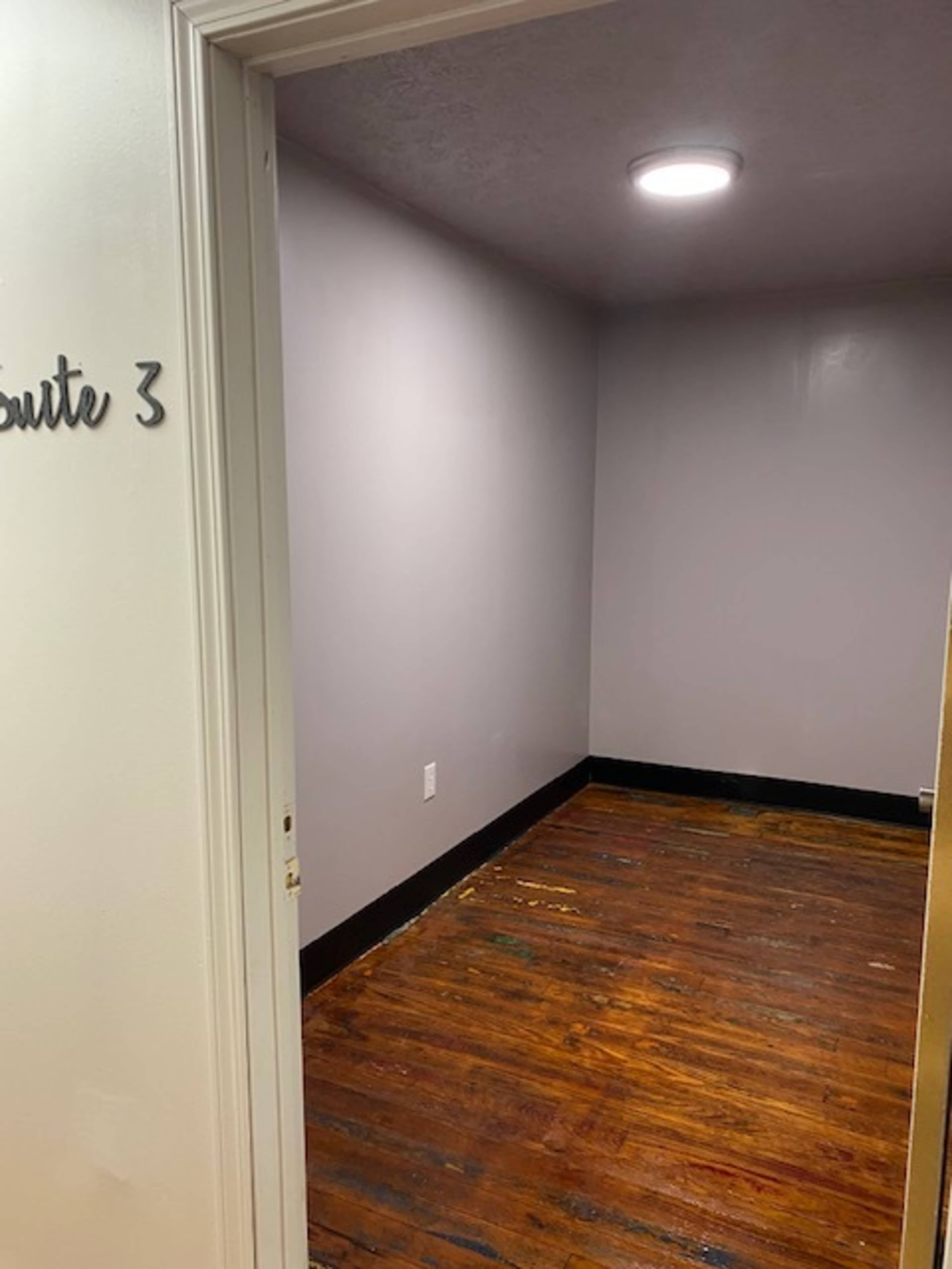 The image shows a small, empty room with gray walls and a wooden floor.