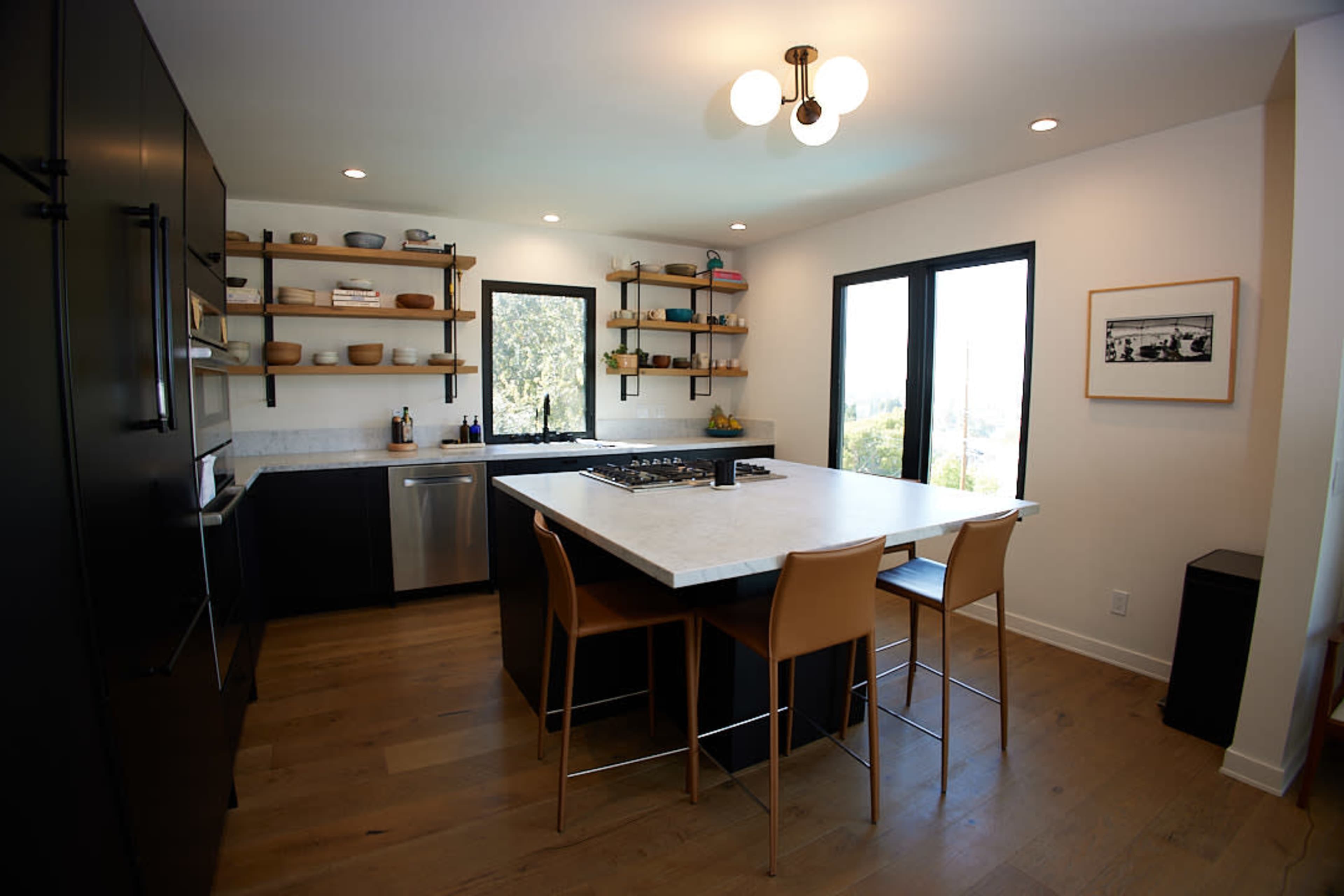 The image shows a modern kitchen featuring black cabinetry, a white countertop, and a central island with four wooden bar stools.