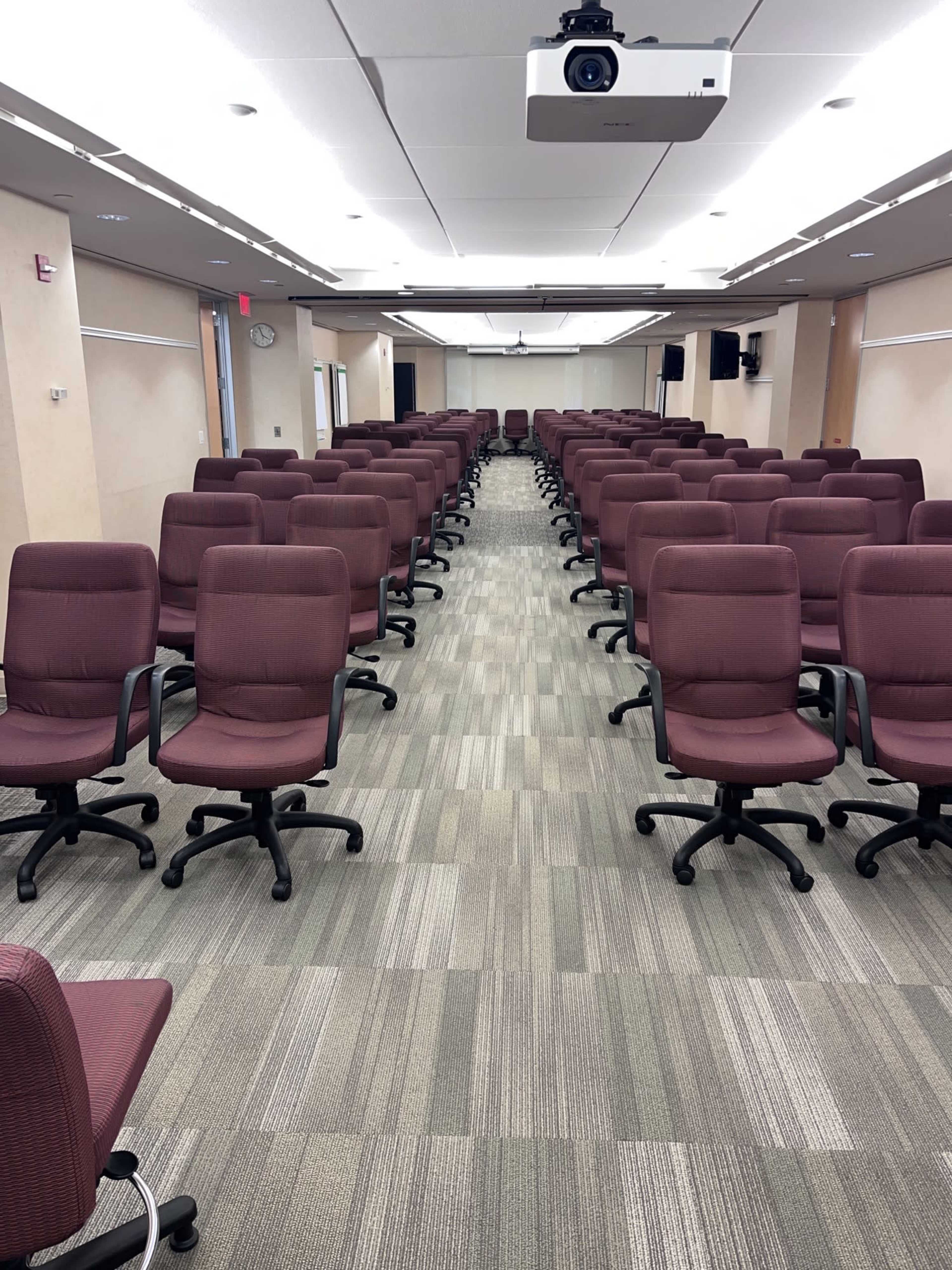 The image shows a conference room with rows of maroon chairs arranged in a linear pattern on a patterned gray floor.
