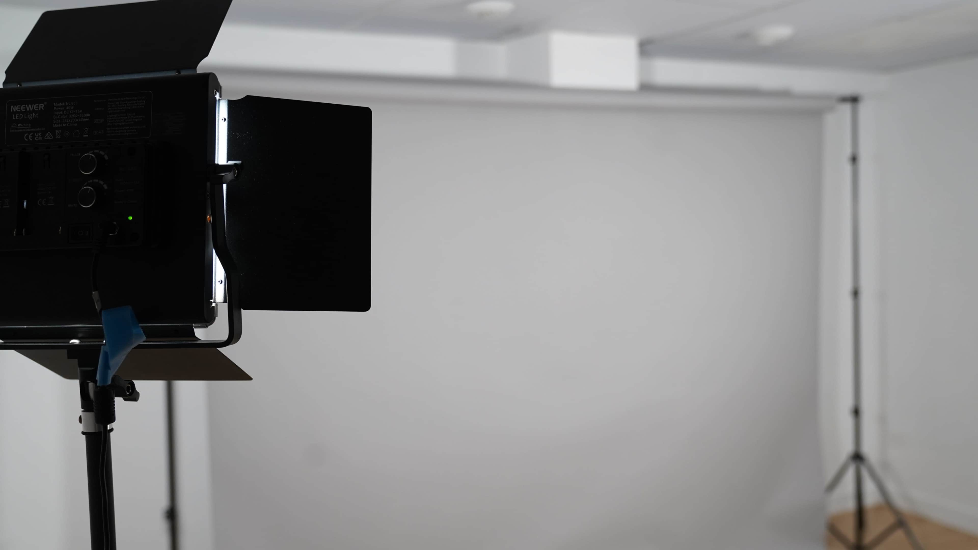 A studio setup features a light source on a stand and a plain backdrop.