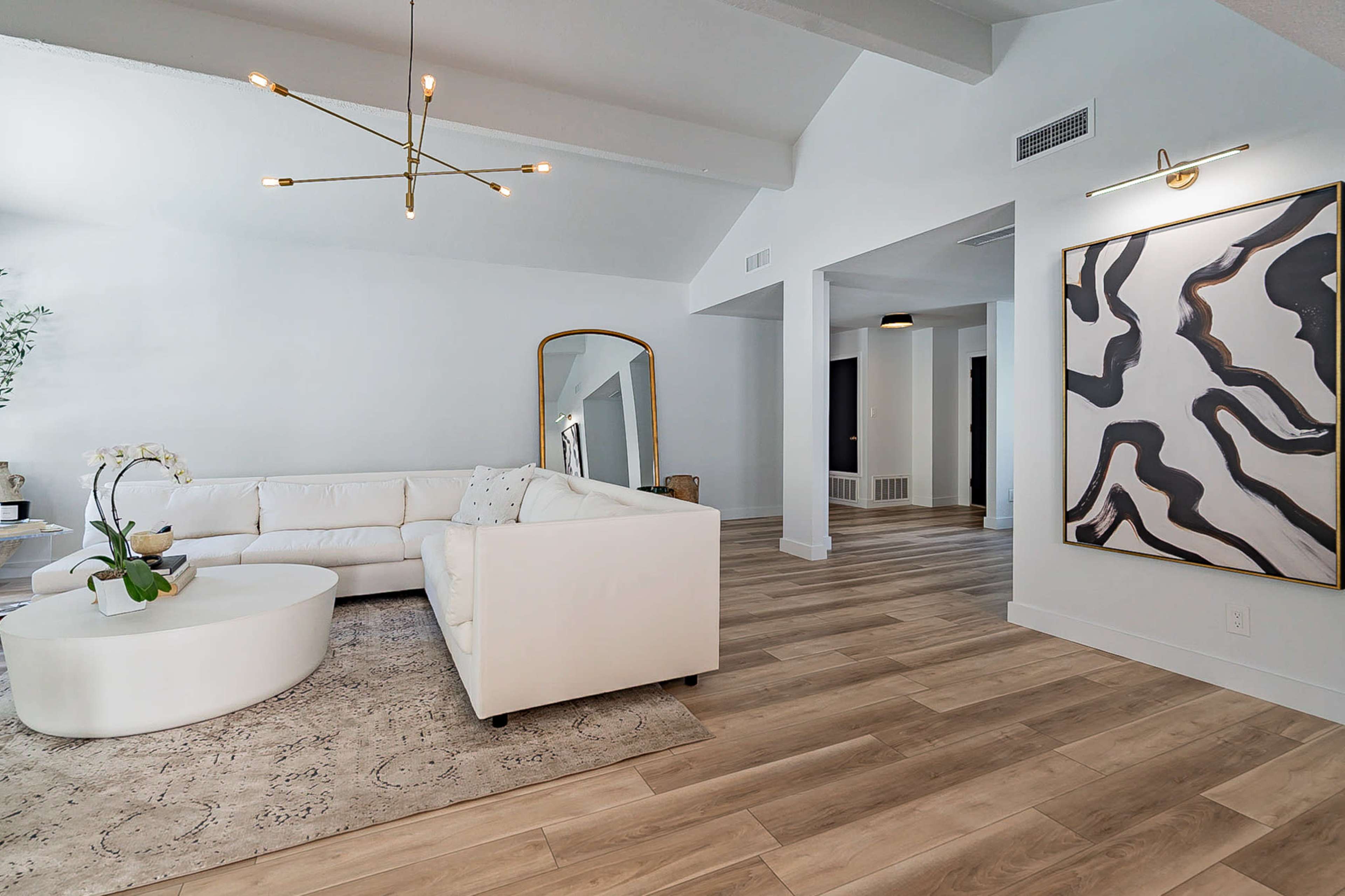 A modern living room with a white sectional sofa, a round coffee table, and a decorative wall art piece, all set on light wooden flooring.